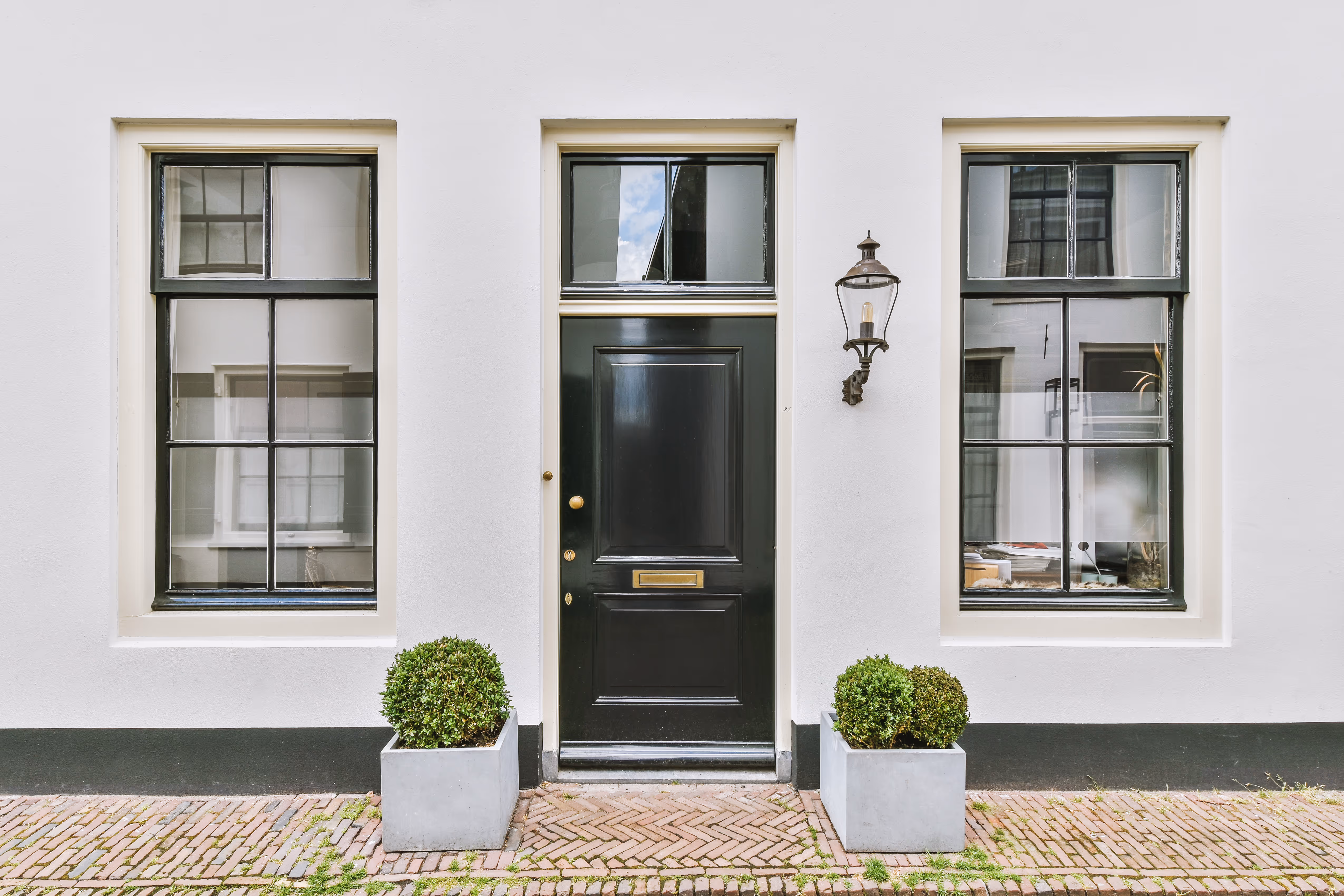 Facade van een witte bakstenen gebouw met een zwarte voordeur en ramen met zwarte kozijnen.