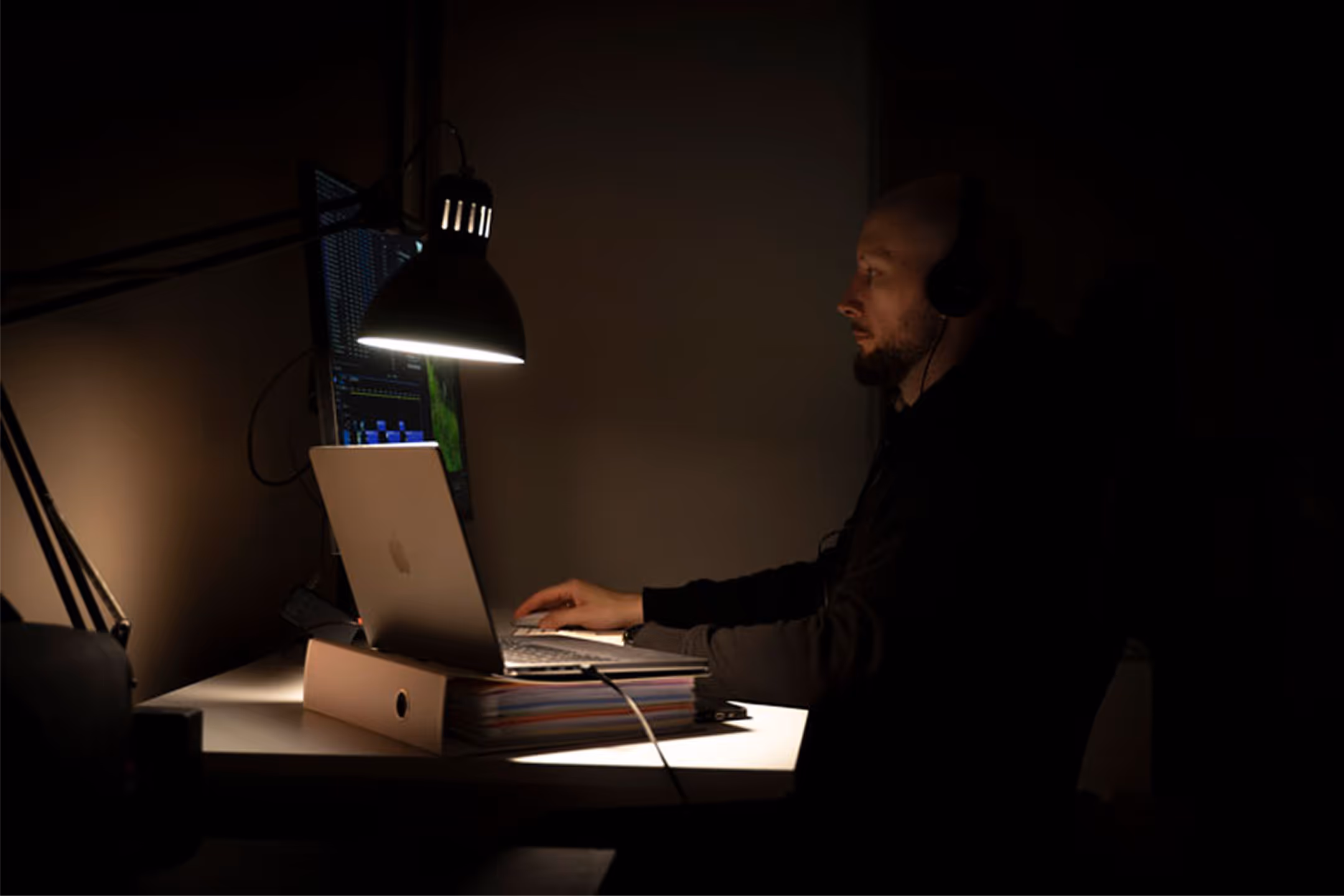 Mateusz Mrozek, projektant stron internetowych, pracujący przy biurku w nocy. Włączony monitor i lampka oświetlają twarz. Zdjęcie symbolizuje proces tworzenia strony internetowej krok po kroku.