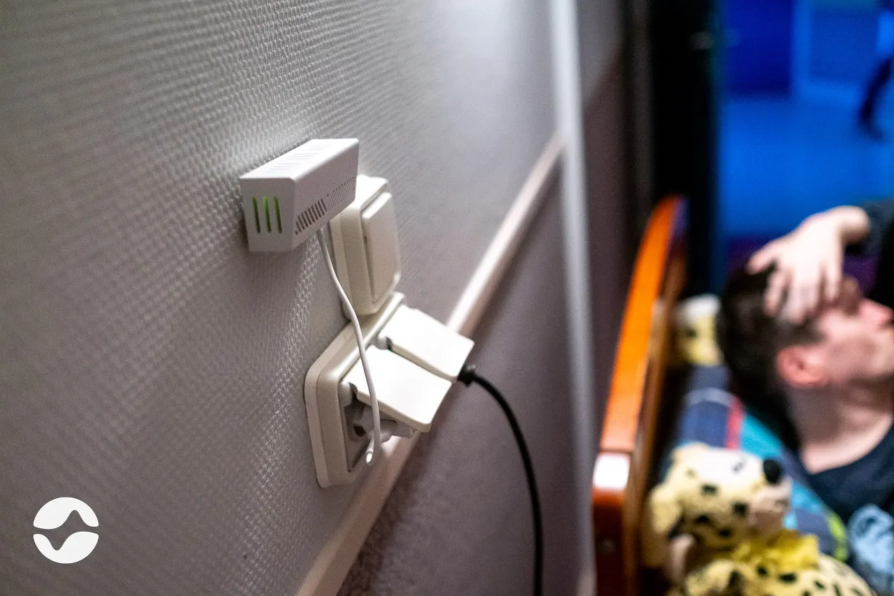 Box connected to the wall of a resident bedroom in MAS, with the resident and a caregiver in the background.