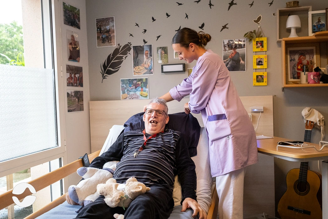 éducatrice spécialisée lors d'un soin en chambre avec un résident dans un établissement handicap.