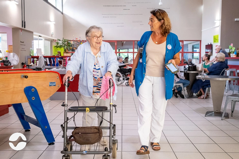 Résidente et aide-soignante qui discutent dans le couloir, smartphone orikio en main.