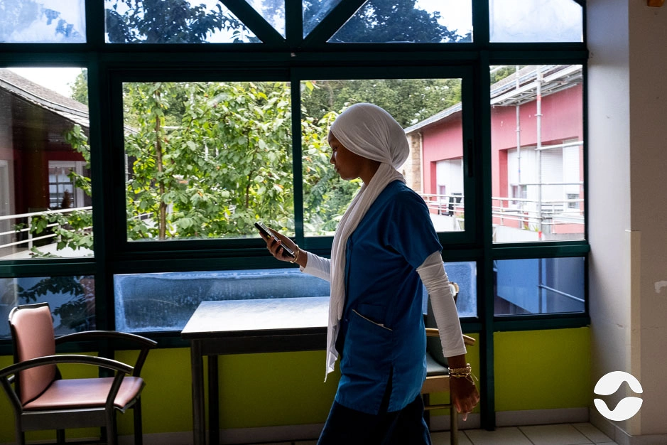 Photo d'une soignante qui passe dans le couloir, téléphone orikio à la main.