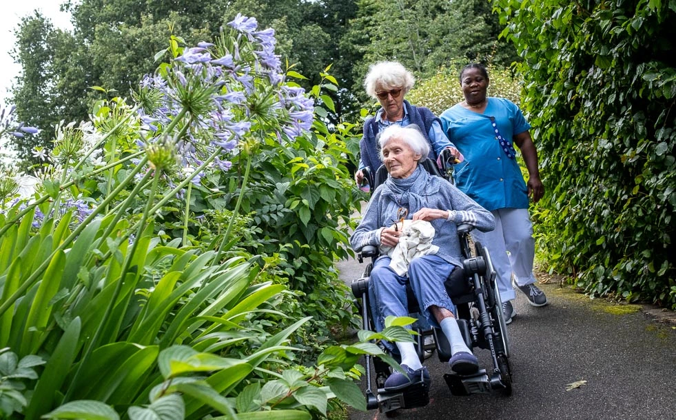 Aide-soignant avec résidentes en salle commune et le boîtier Orikio en fond.