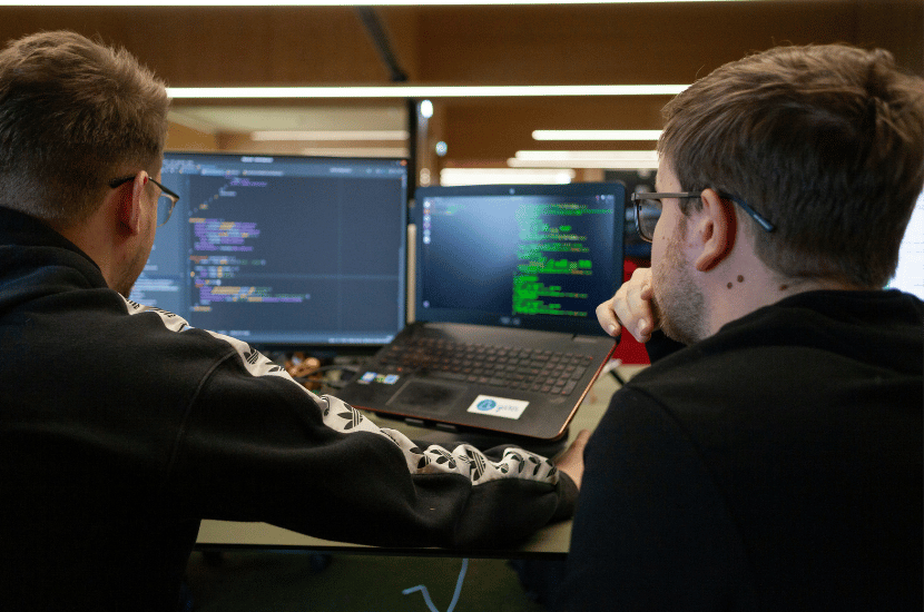 Two software developers collaborating on code at their workstations, representing teamwork in software construction and application development.