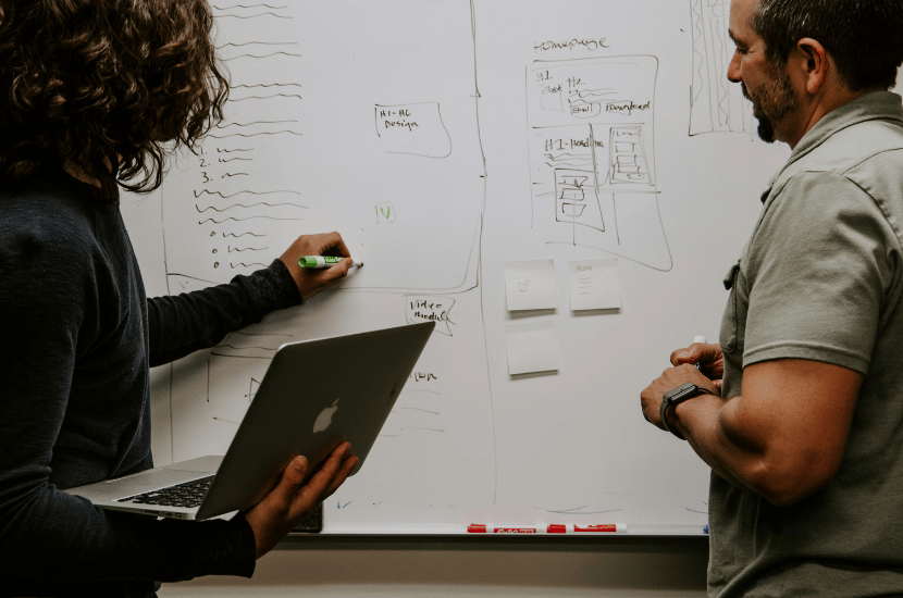 Two business analysts collaborating at a whiteboard, mapping out process flows and strategic solutions during a planning session.