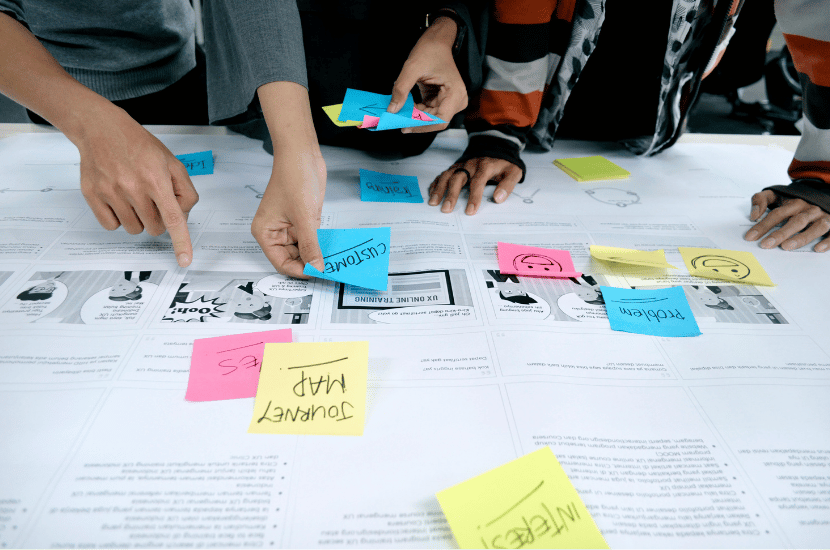 A diverse design team reviewing brand and interface mockups on a table, using colorful sticky notes to annotate improvements during a collaborative workshop.