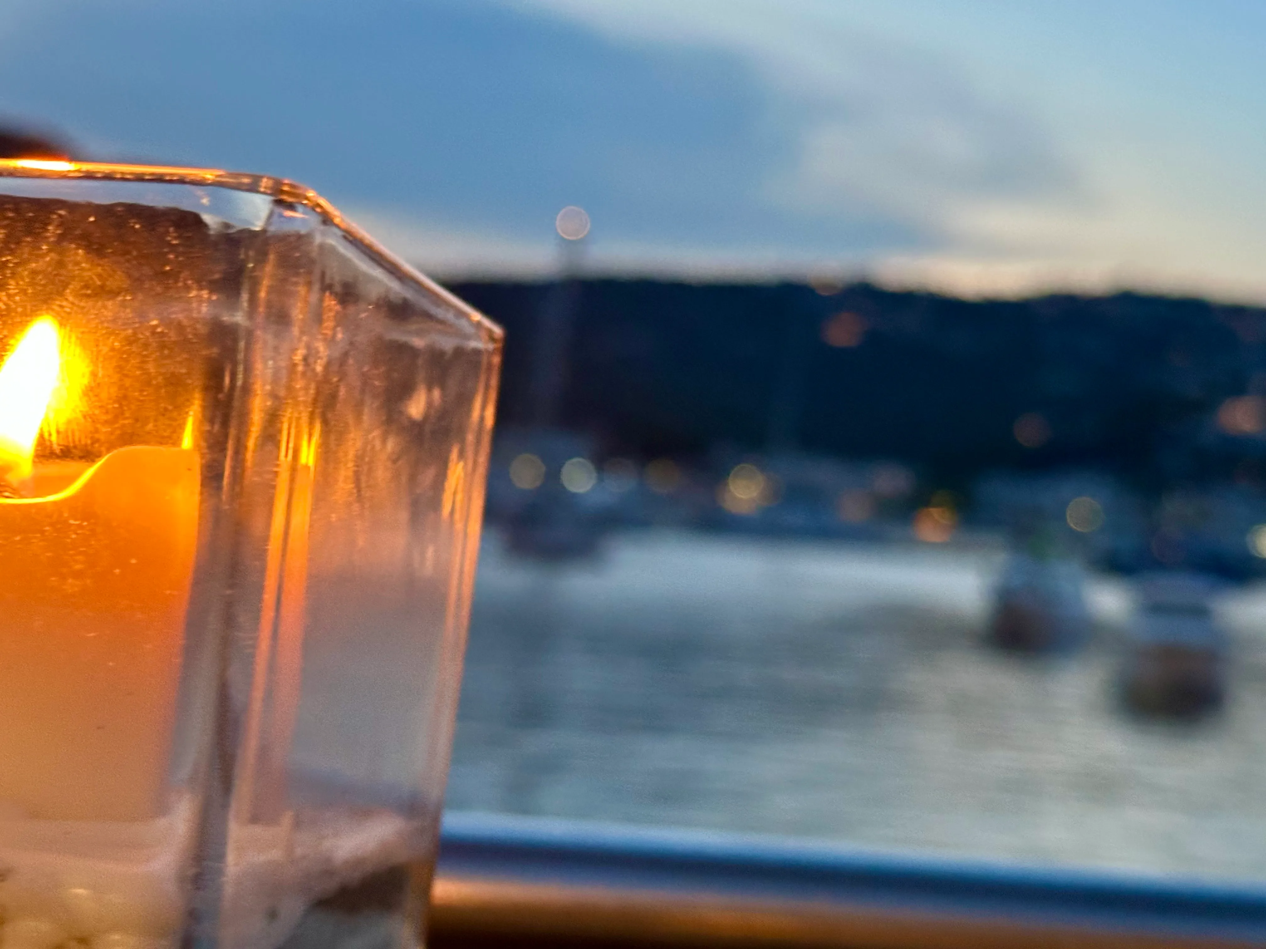 Glowing candle by window with blurred cityscape and water in background