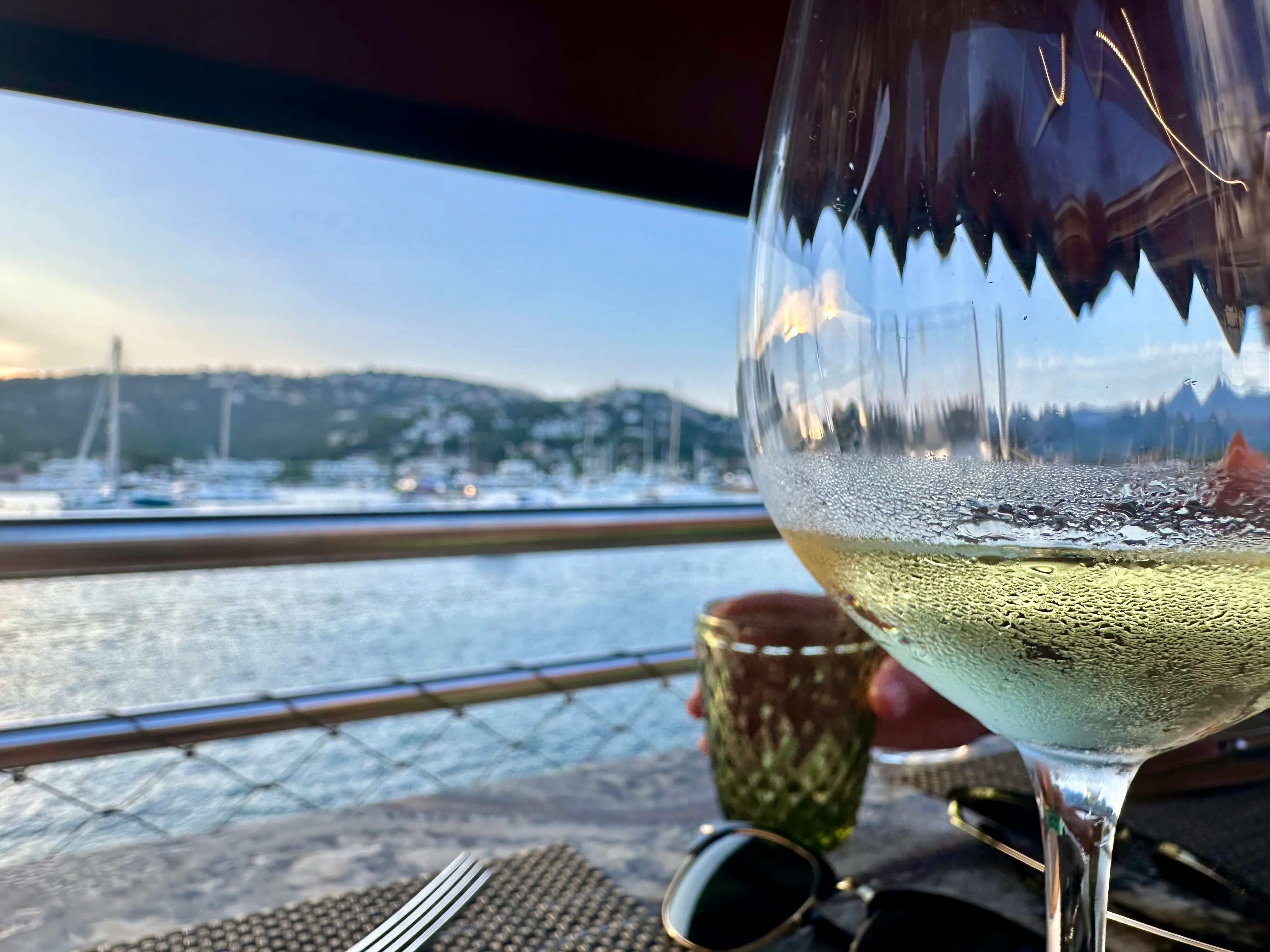 Condensation-covered wine glass with marina and sailboats in background