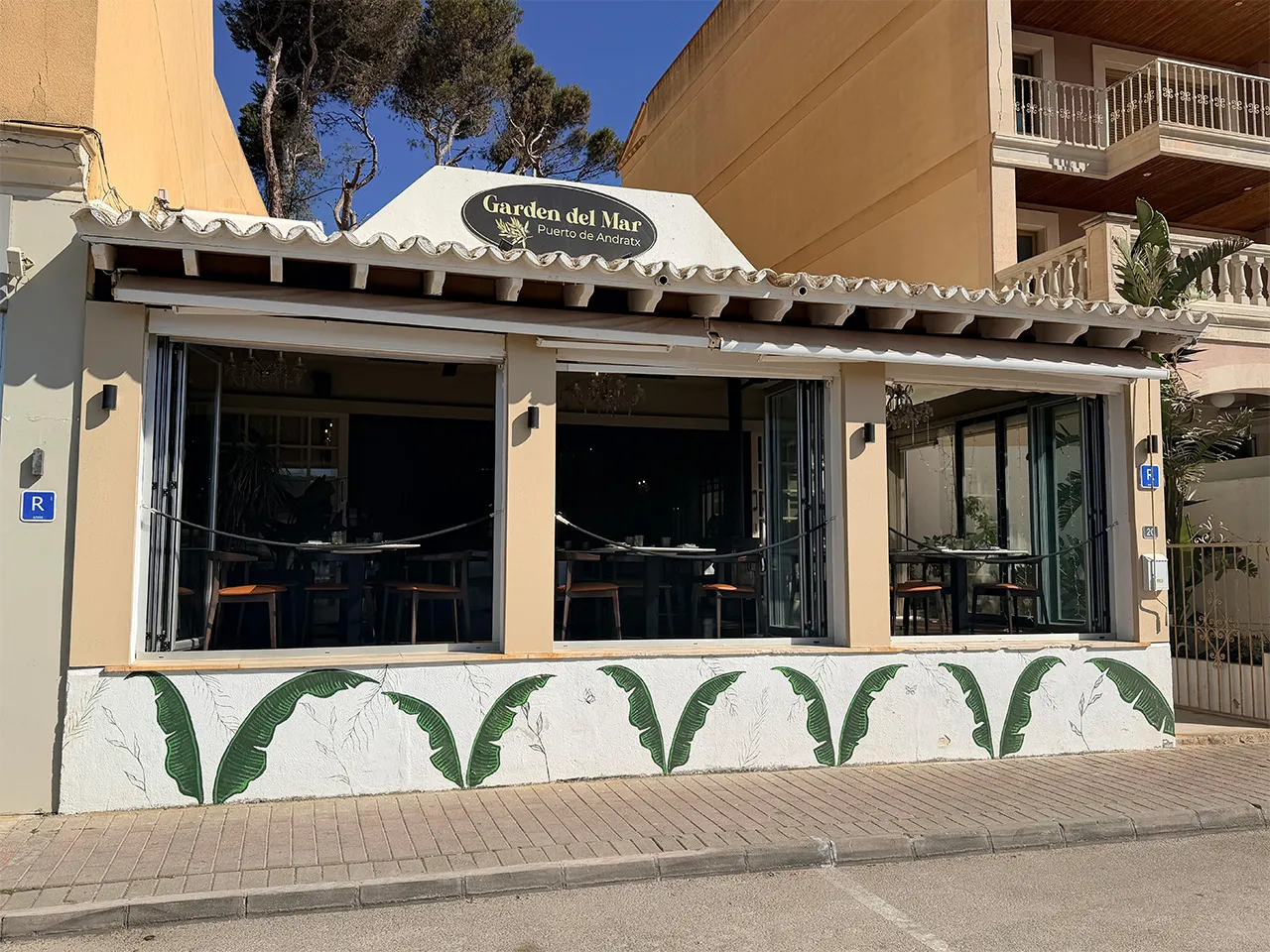 Exterior of Garden del Mar restaurant with open windows and green leaf mural on white wall.