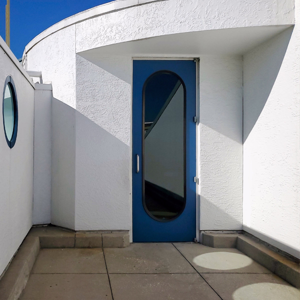 Modern blue entrance door with arched glass panel on a white building