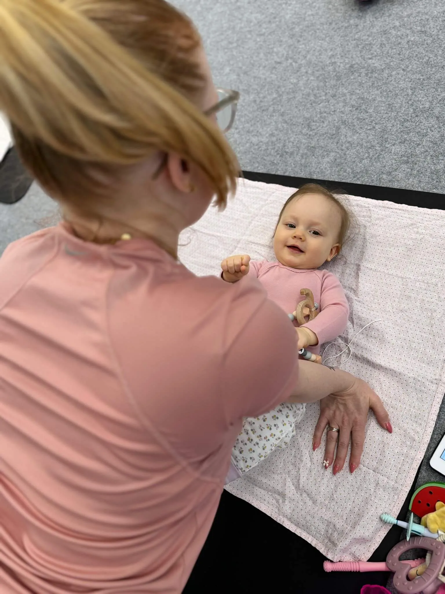 Baby liegt entspannt auf Matte, Mama hält sanften Kontakt im Yoga.