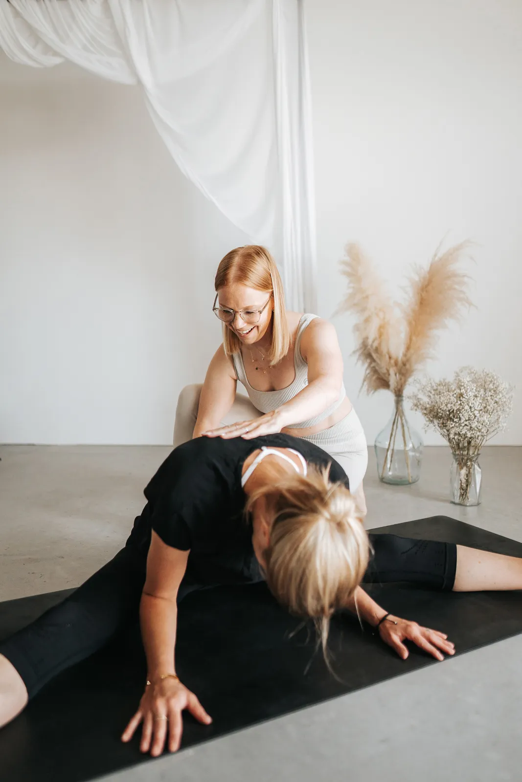 Yoga Lehrerin gibt einer Teilnehmerin sanfte Hilfestellung in einer Dehnung – Hatha Yoga in Melk, Niederösterreich.