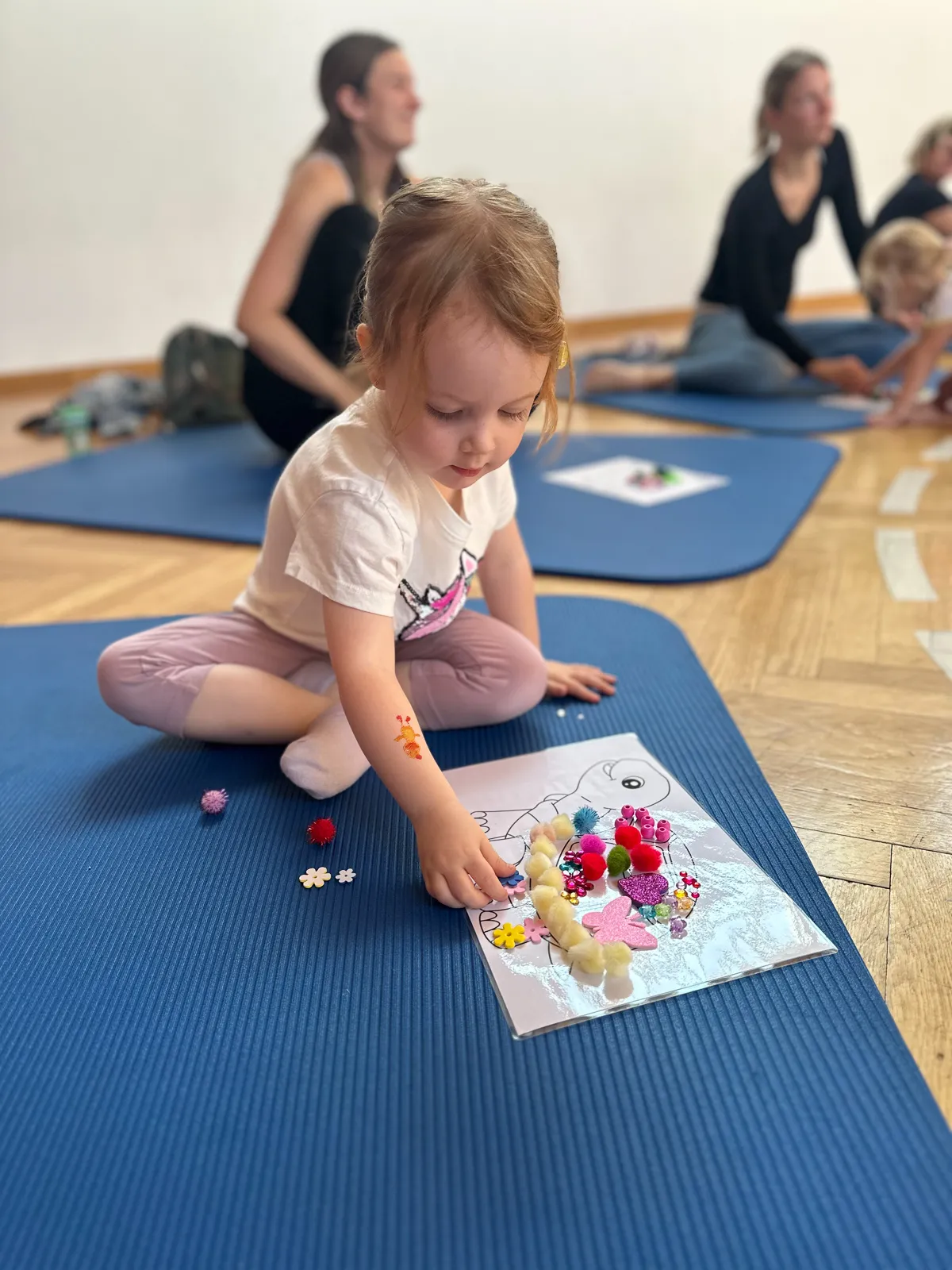 Kind legt ein Bild mit bunten Kugeln -Kreatives Basteln auf der Yogamatte.