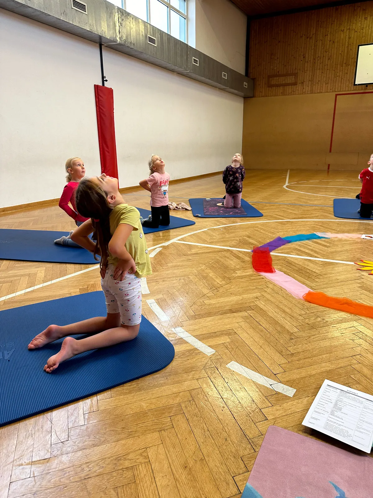 Kinder üben die Kamel-Pose gemeinsam.