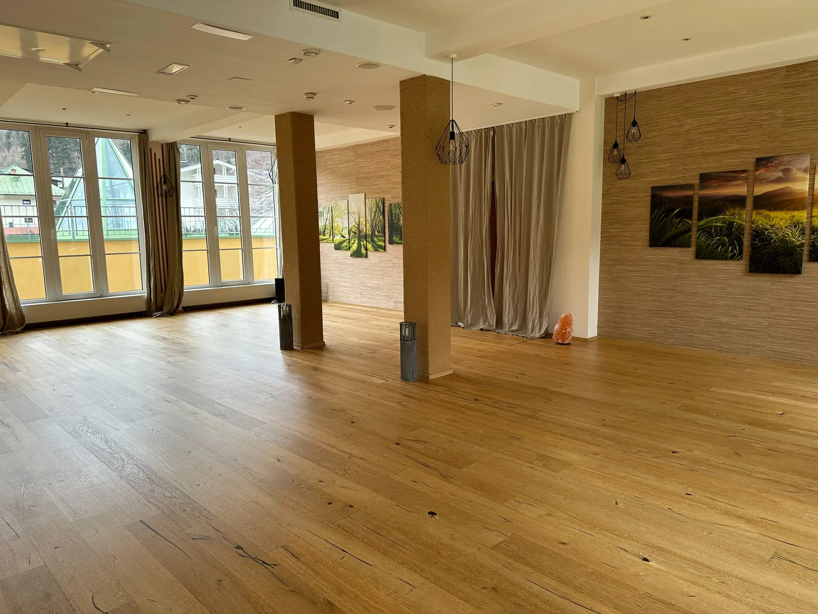 Großer Yogaraum mit Holzboden, großen Fenstern und Naturbildern, perfekt für Yoga-Retreats.