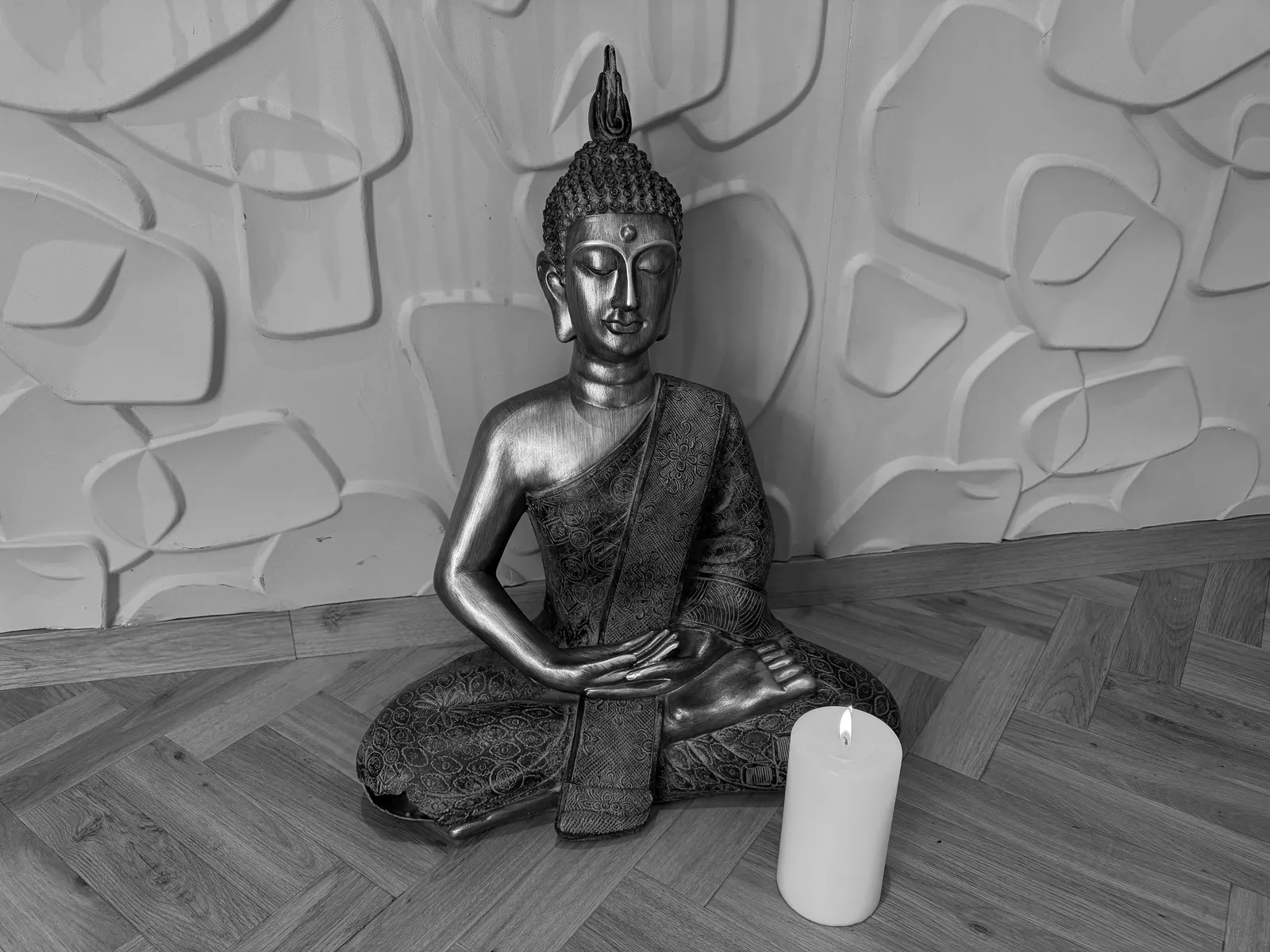Schwarz-weiß Aufnahme einer Buddha-Statue mit Kerze, Symbol für Meditation und Achtsamkeit.