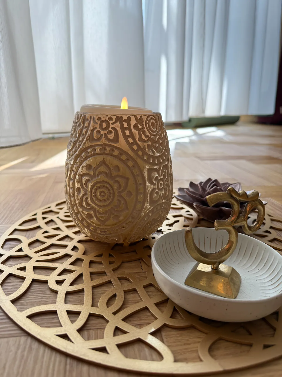 Detailaufnahme einer brennenden Kerze in verziertem Halter auf einem goldenen Tablett, Symbol für Achtsamkeit.