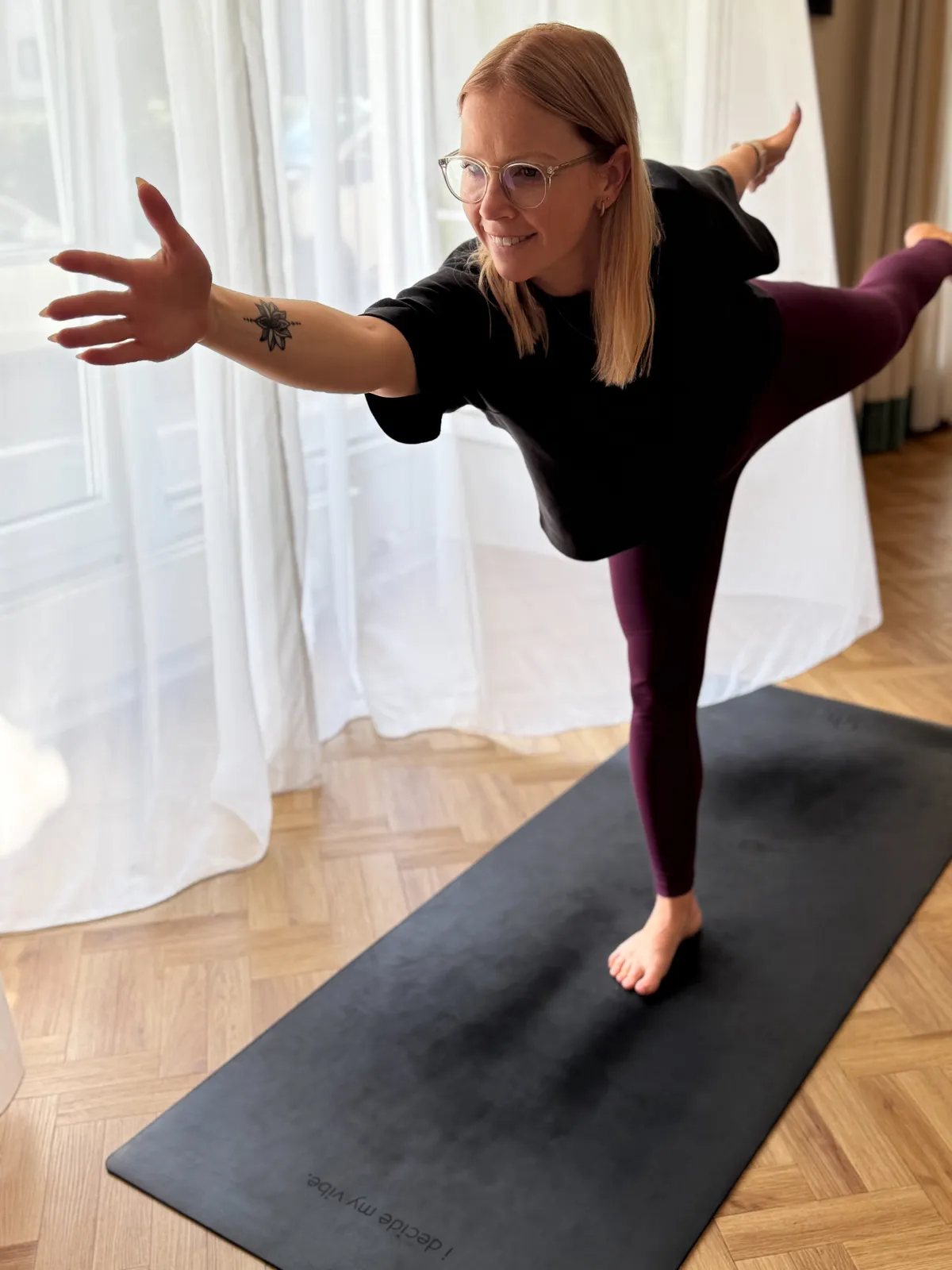 Yogalehrerin übt die Krieger-III-Haltung auf einer Matte im hellen Yogaraum.
