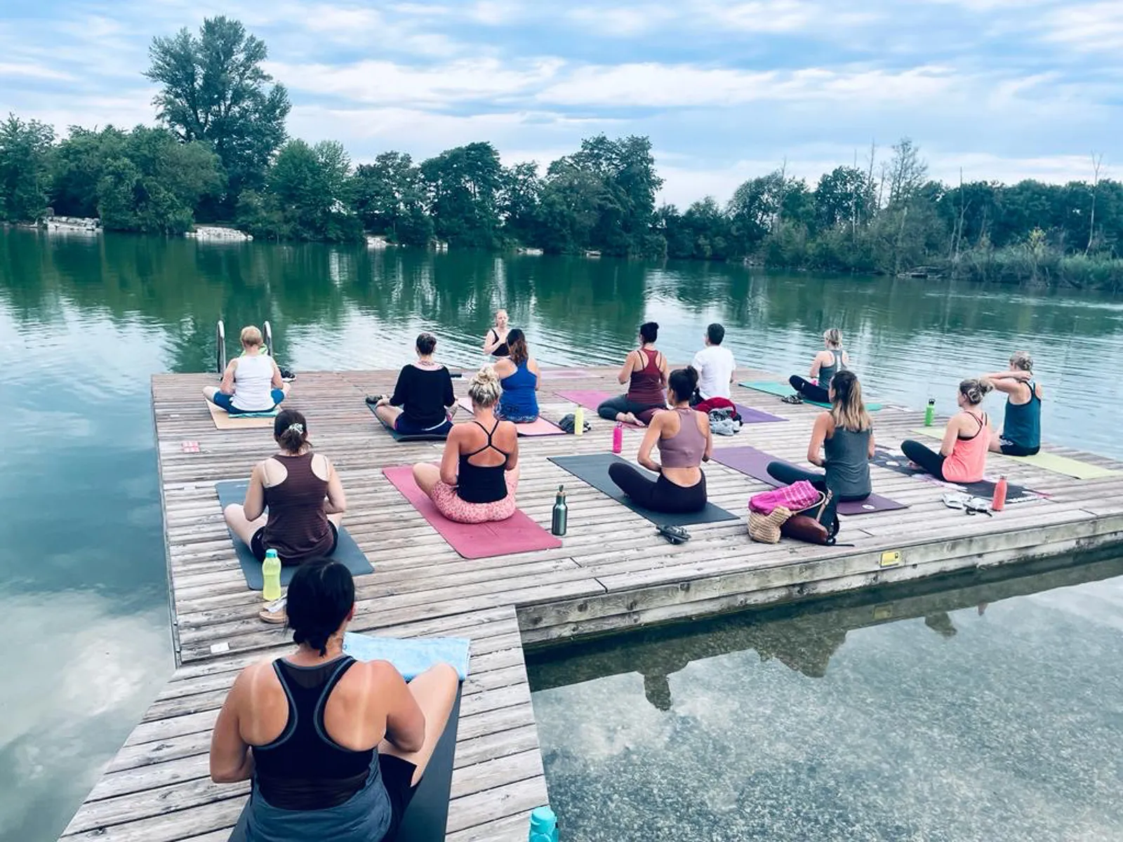 Yoga-Gruppe meditiert im Schneidersitz auf dem Steg am Ebersdorfersee.