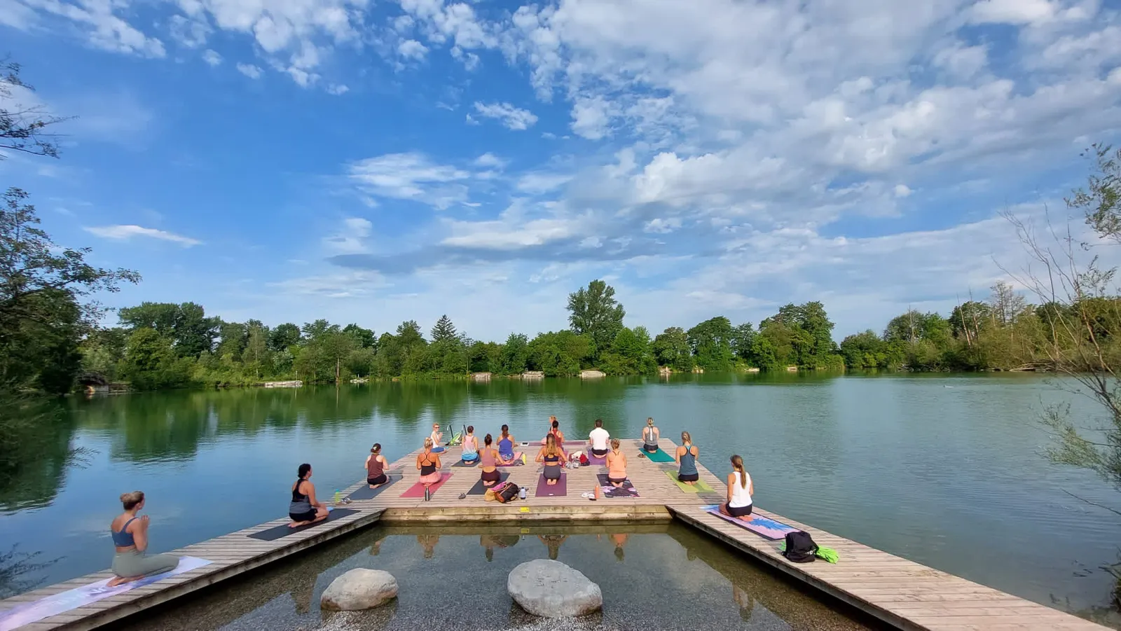 Yoga-Gruppe sitzt am Steg des Ebersdorfersees für Sunrise-Yoga in Niederösterreich.