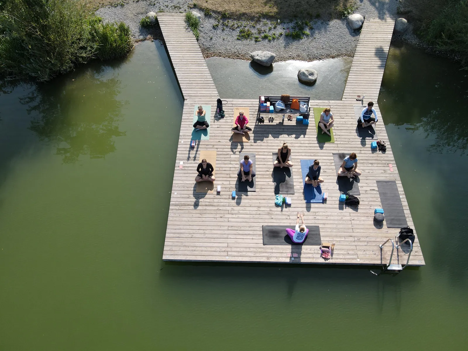 Yoga-Stunde am Steg des Ebersdorfersees von oben fotografiert, Gruppe in Meditationshaltung.