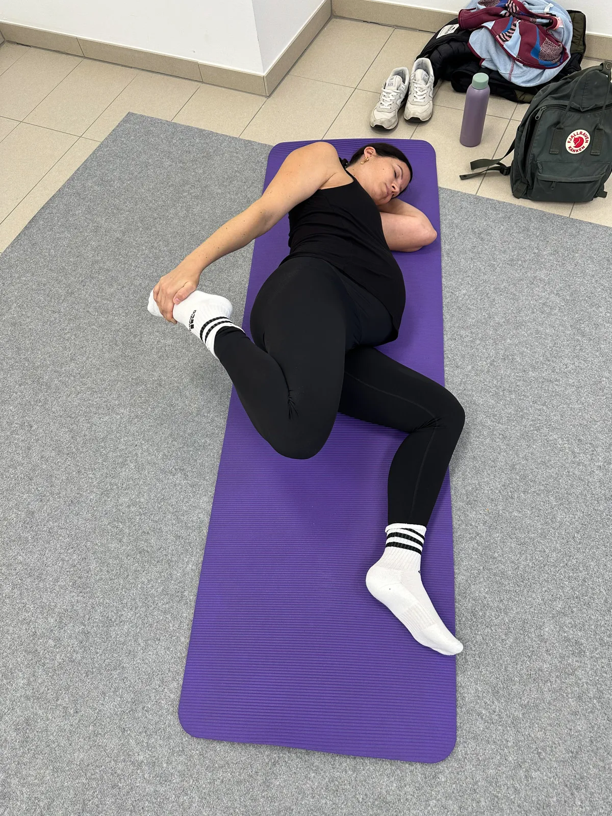 Schwangere Frau liegt entspannt auf der Yogamatte in Seitenlage, sanfte Dehnung und Entspannung beim Schwangerschaftsyoga.