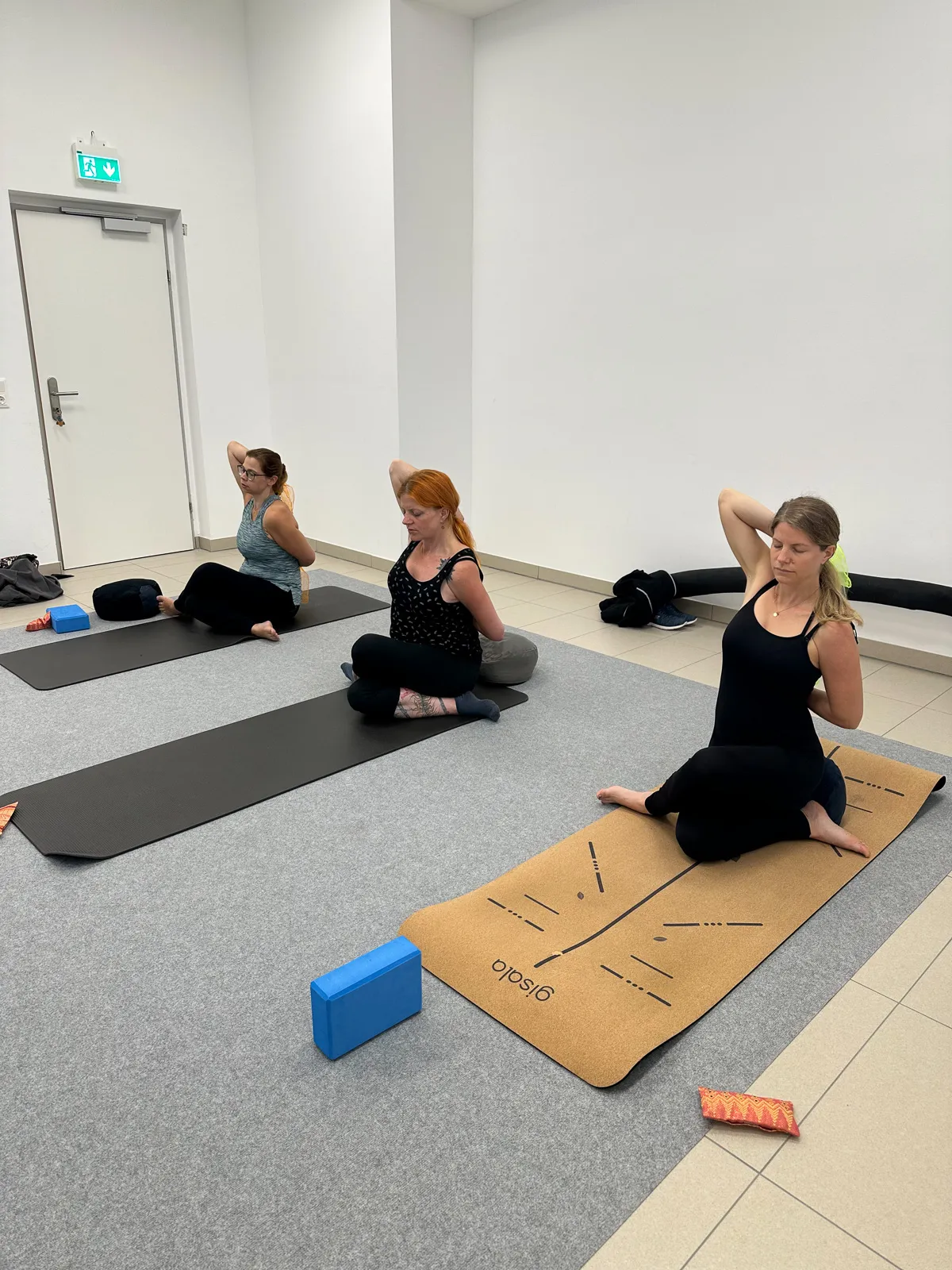 Mehrere schwangere Frauen sitzen auf Yogamatten und üben Schulter- und Brustöffnung während eines Schwangerschaftsyoga-Kurses.