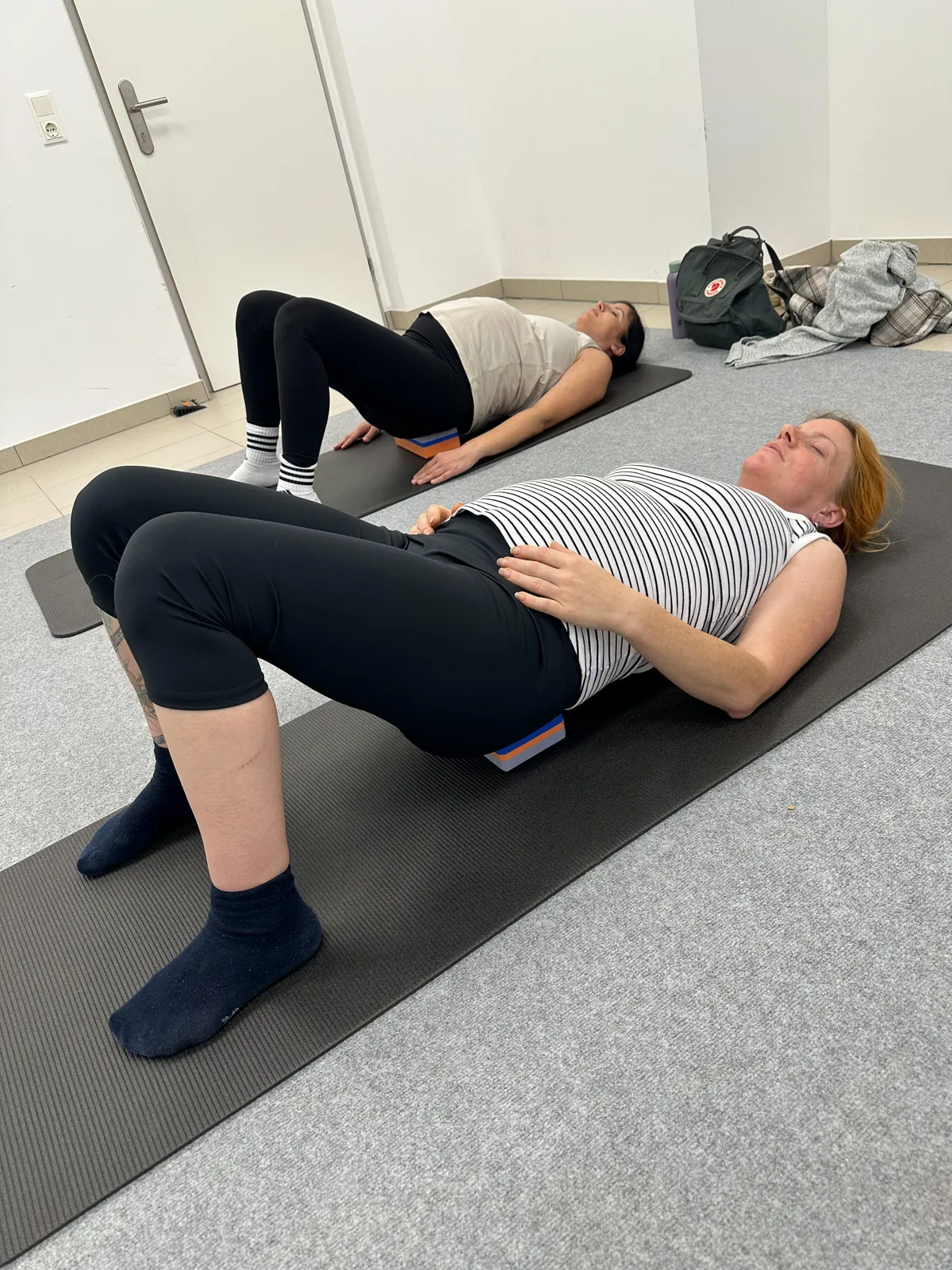 Zwei Schwangere liegen auf der Matte und machen sanfte Beckenbodenübungen zur Vorbereitung auf die Geburt im Yoga-Kurs.
