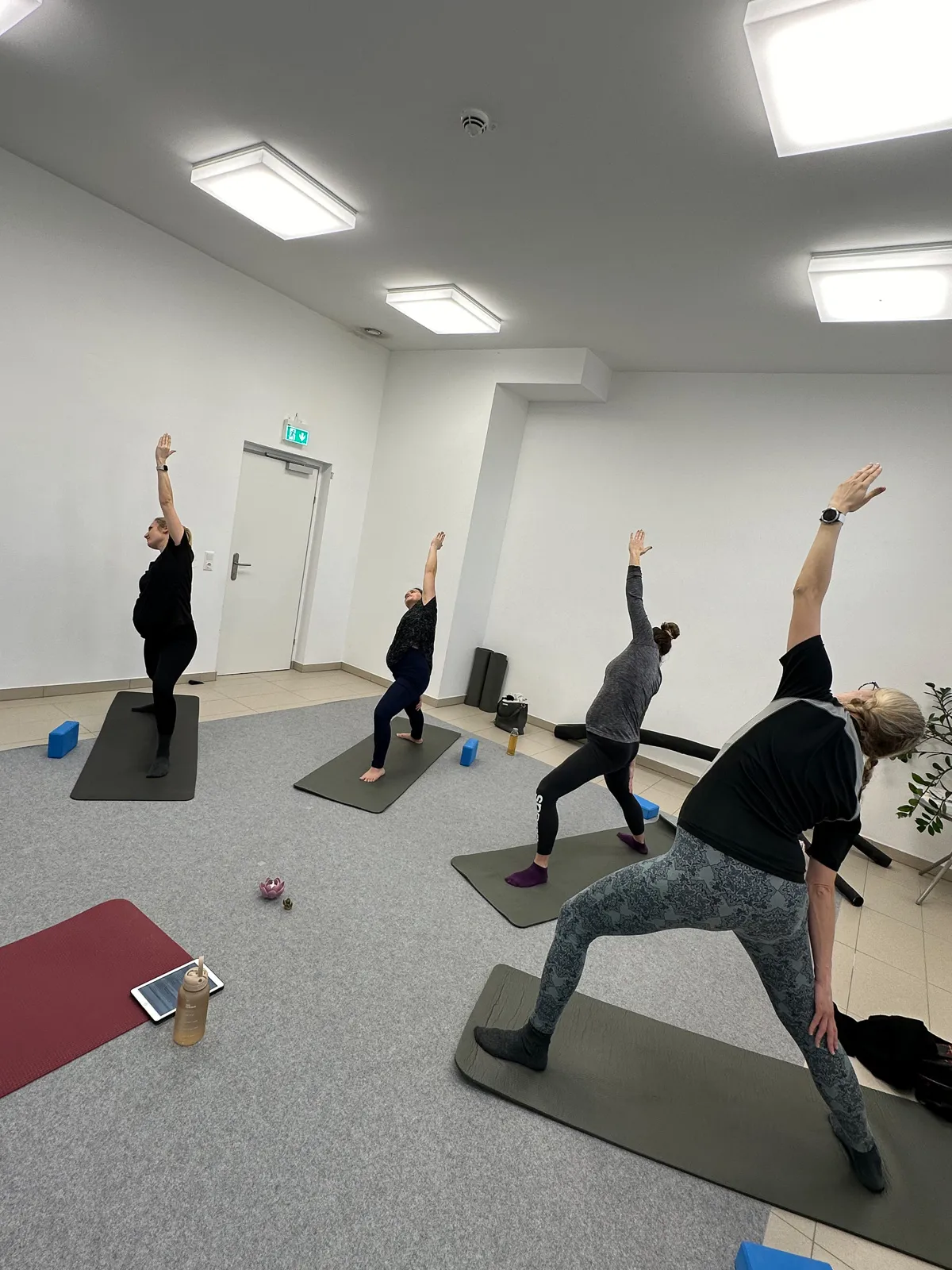 Schwangere Frauen üben gemeinsam die Kriegerhaltung im Schwangerschaftsyoga-Kurs, Fokus auf Kraft, Balance und Achtsamkeit.