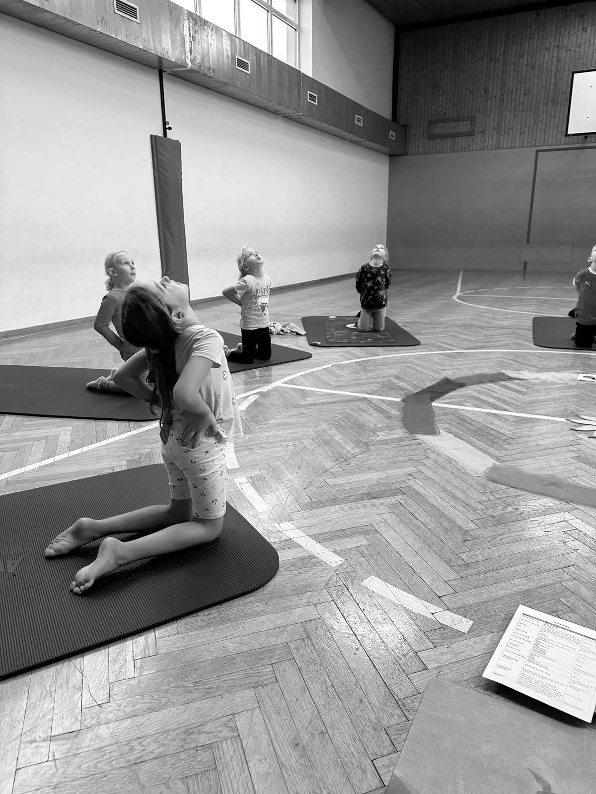 Mehrere Kinder machen Yogaübungen auf Matten in einer Turnhalle und üben Achtsamkeit durch Bewegung.