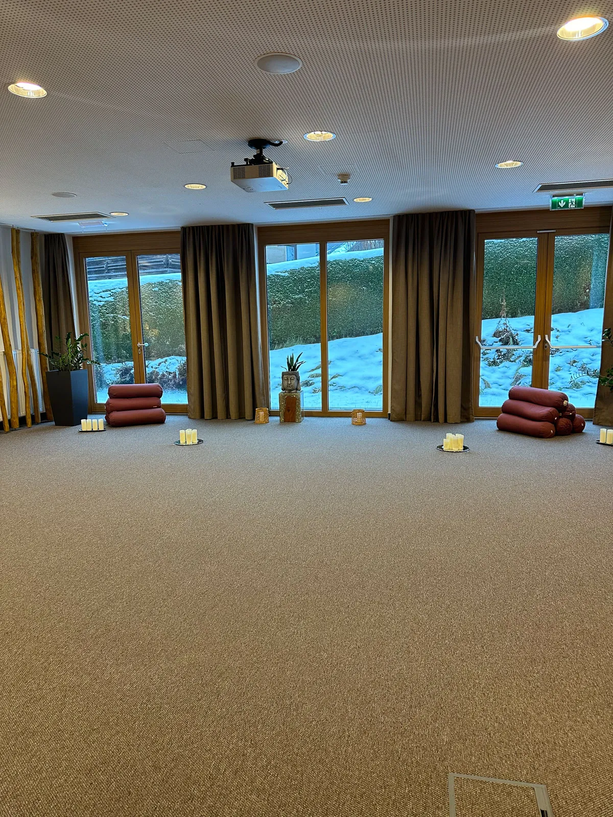 Heller Yoga-Raum mit Matten, Kissen und Kerzen, Blick auf verschneite Landschaft – ideal für Retreats und Entspannung
