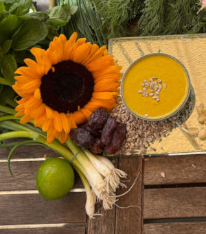 a photo of a bowl of saffron and sunflower seed dressing next to some vegetablles and sunflower seeds