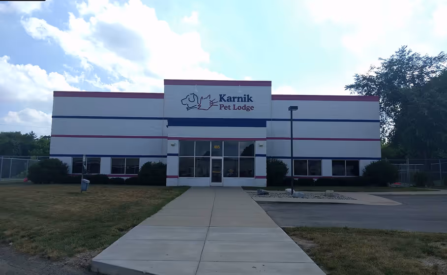 Front view of Karnik Pet Lodge building with a paved walkway leading to glass entrance doors under a partly cloudy sky.