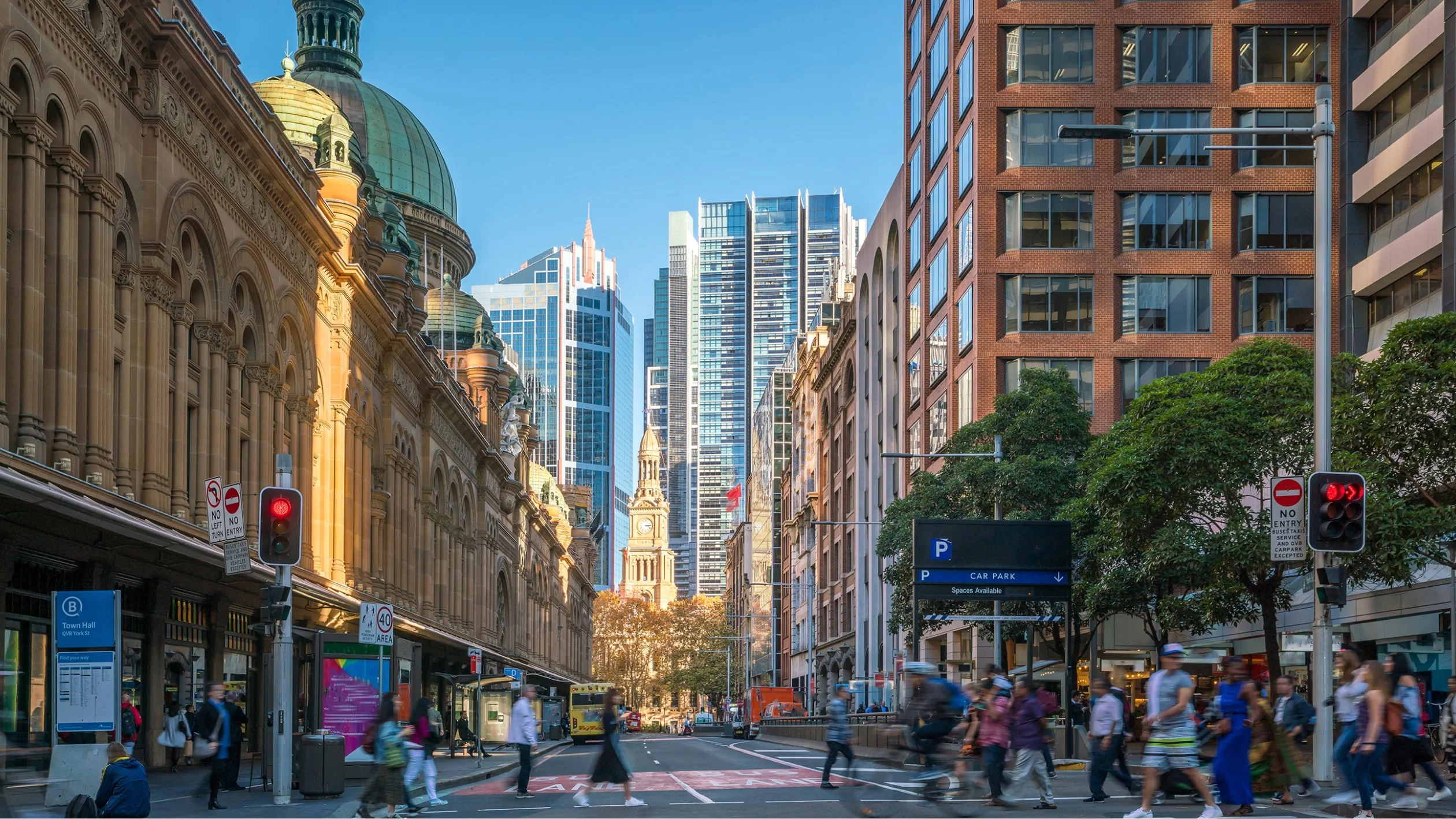 A bustling city street filled with pedestrians walking and cars navigating through traffic.