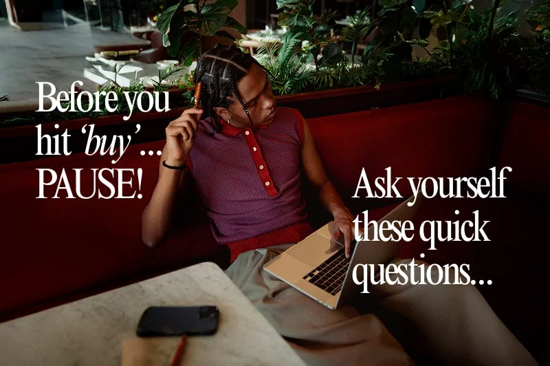 A person sits on a red bench using a laptop, with a phone and keys on the table. Overlaid text reads: "Before you hit ‘buy’... PAUSE! Ask yourself these quick questions...