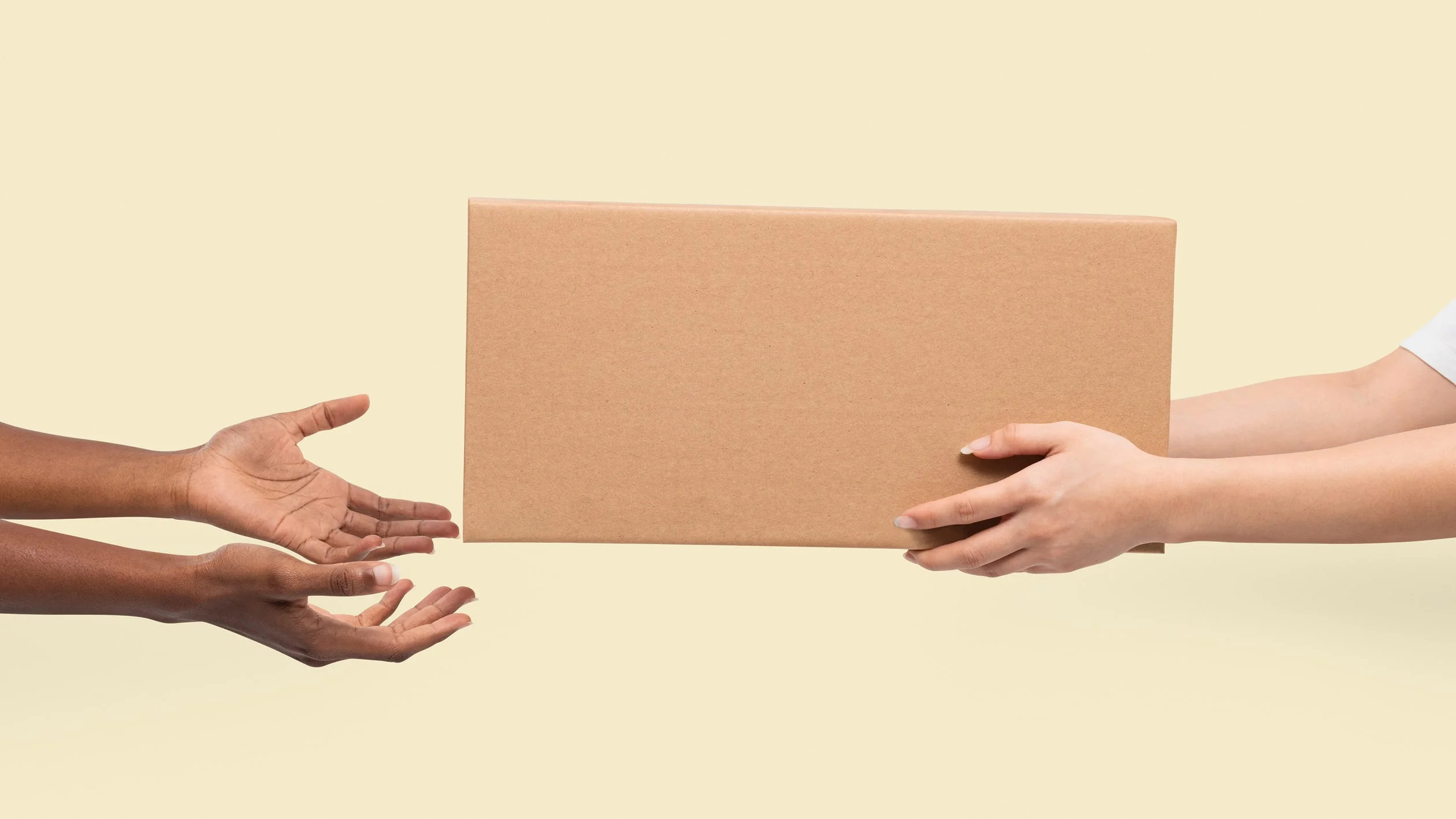 One person hands a rectangular cardboard box to another person against a plain light background.