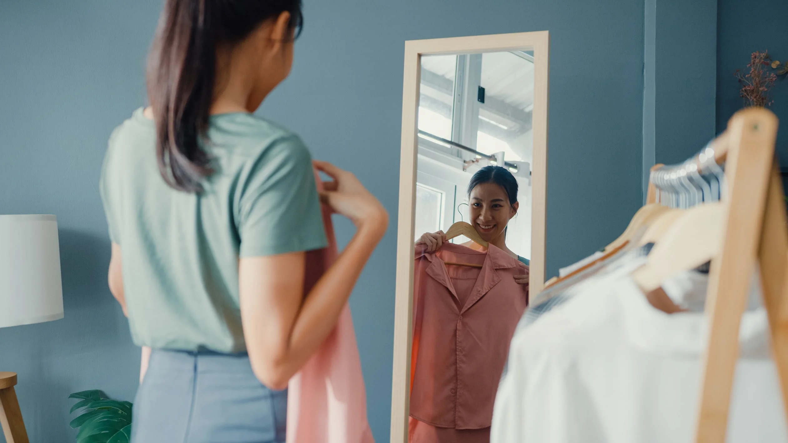A woman gazes at her reflection in a mirror, assessing her outfit with a thoughtful expression.