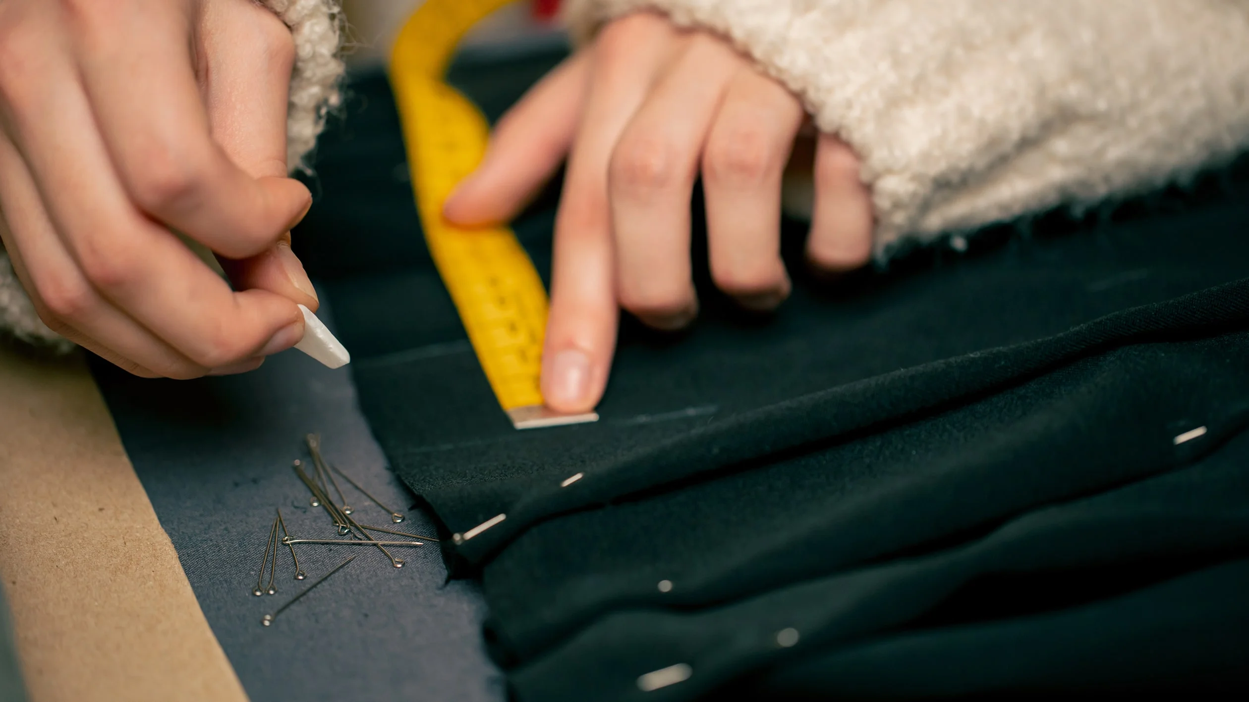 A person cuts fabric while measuring it with a tape measure, focused on precise measurements for their project.