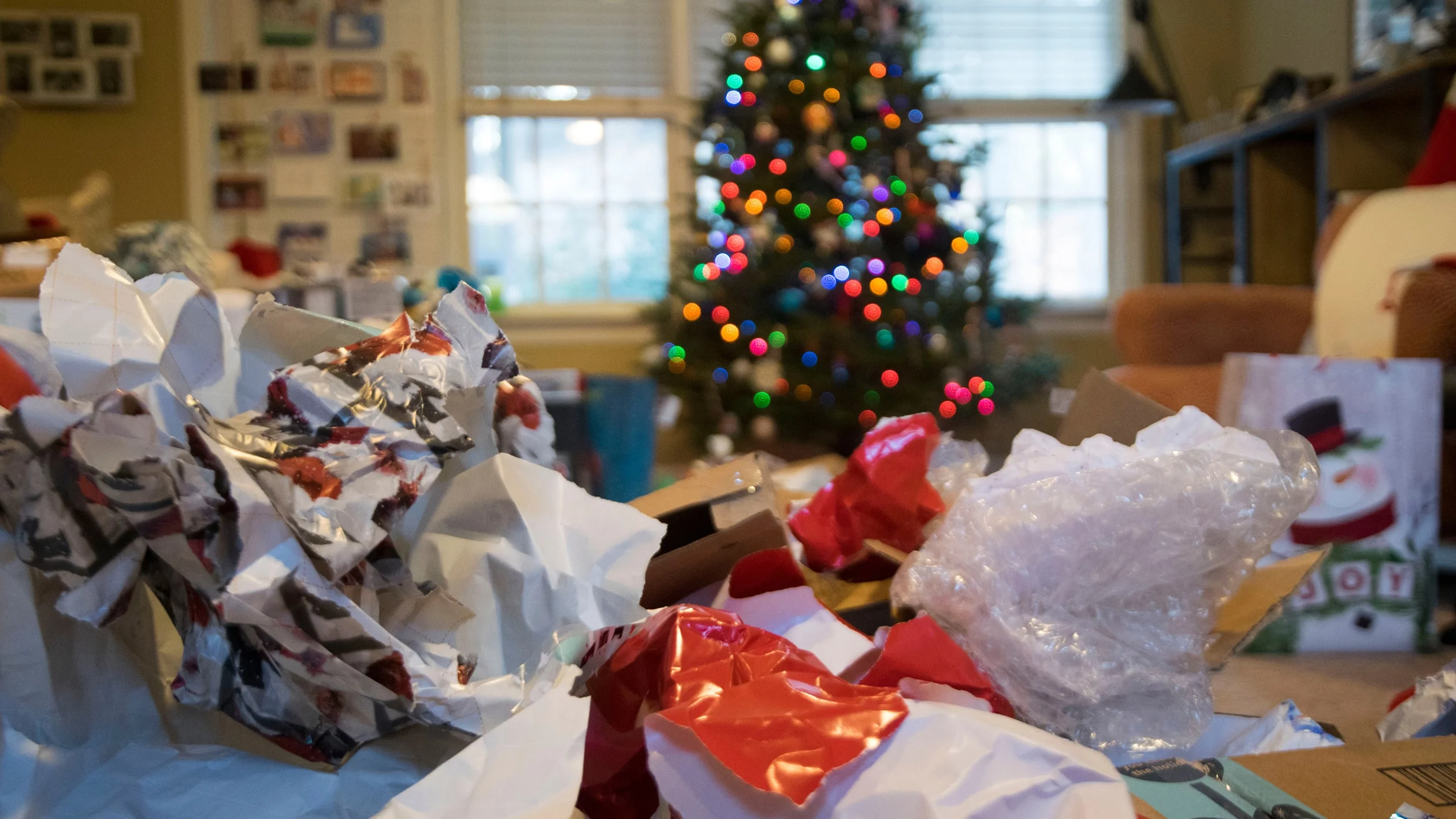 A cluttered living room filled with colorful Christmas decorations and wrapped gifts scattered around the space.