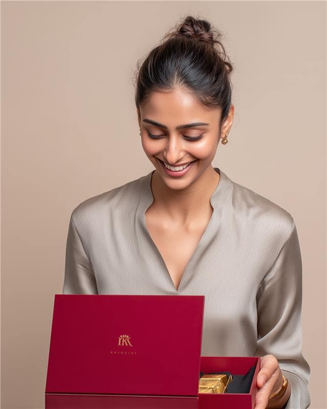 Smiling woman with hair in a bun holding an open red gift box with gold chocolates inside.