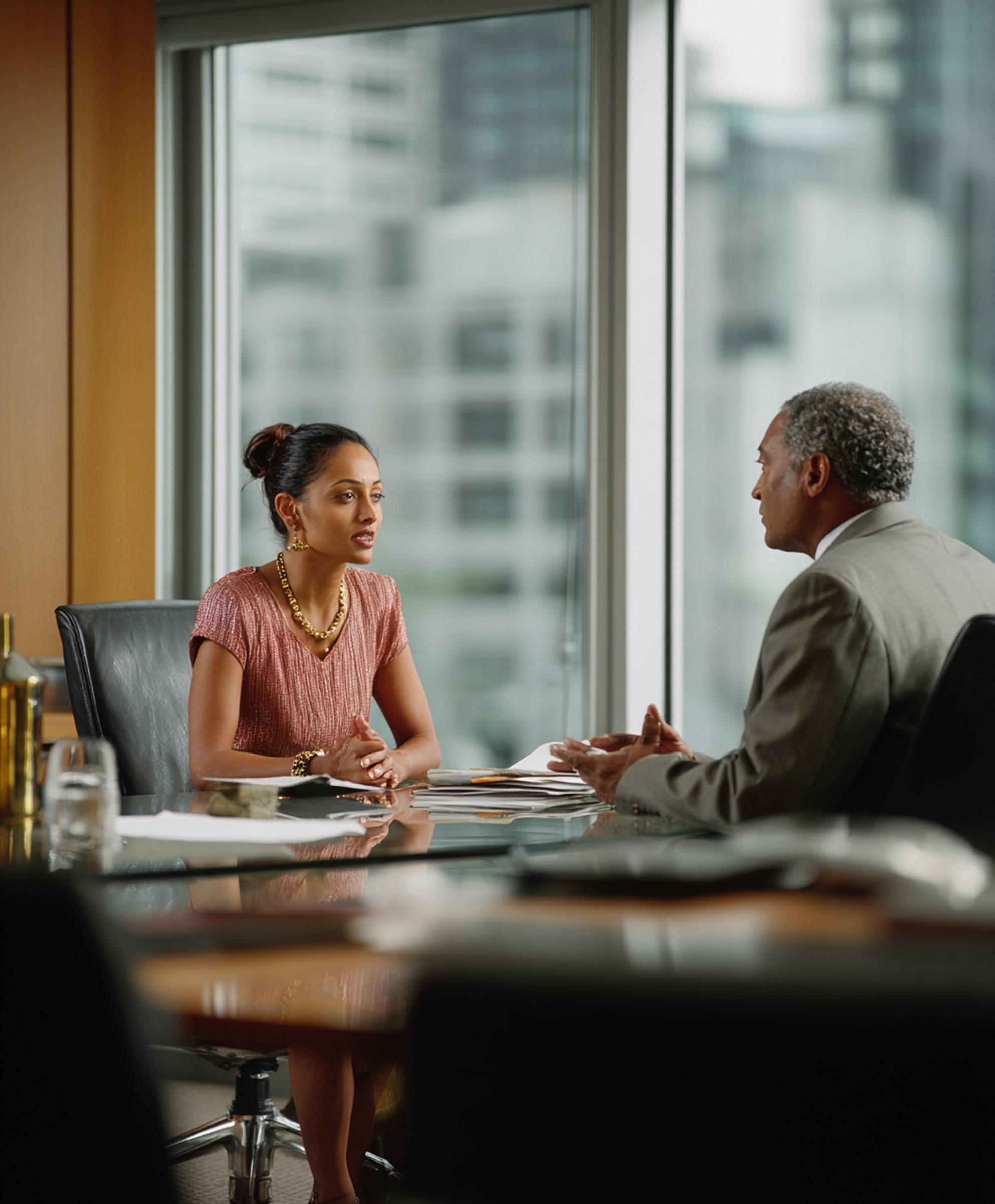 A woman and a man in business attire engaged in a discussion across a conference table in a modern office.