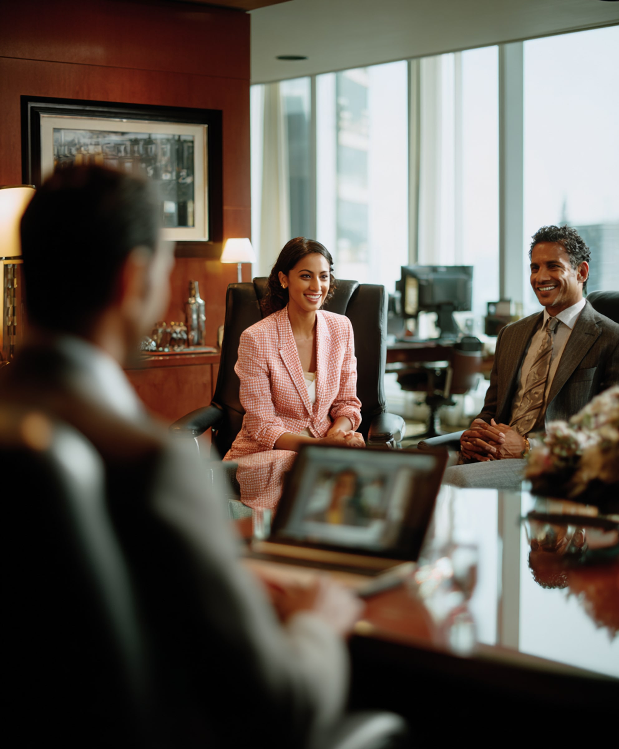 Two business professionals smiling and sitting across from a third person in an office with large windows and wooden walls.