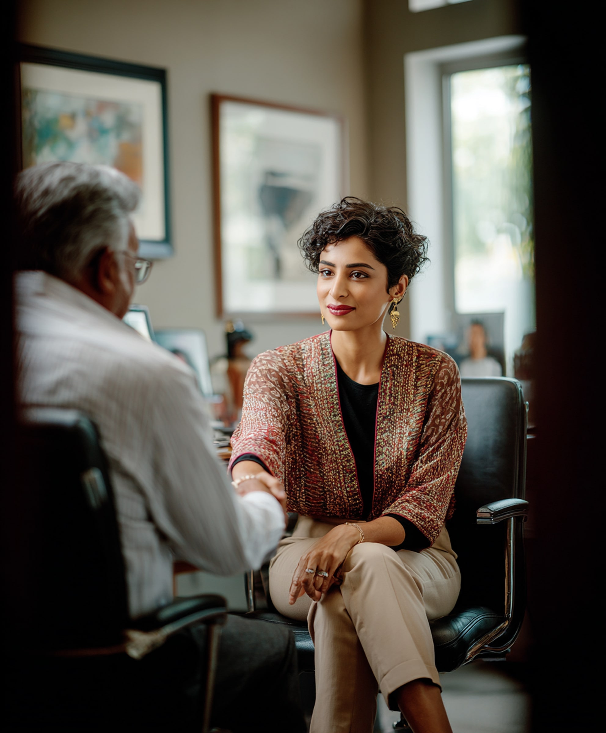 Woman with short curly hair shaking hands with a man in an office setting.