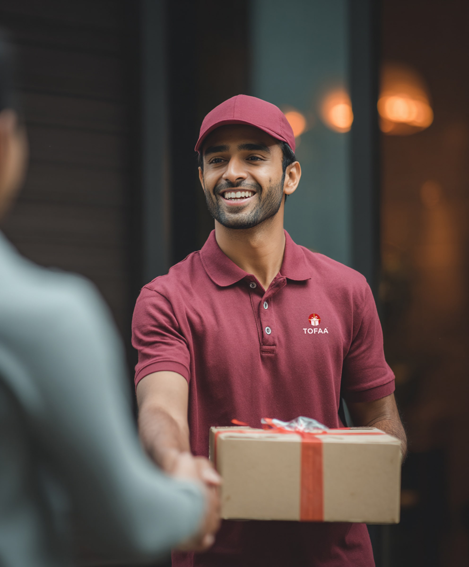 Smiling delivery man in maroon uniform handing a gift-wrapped package during a handshake.