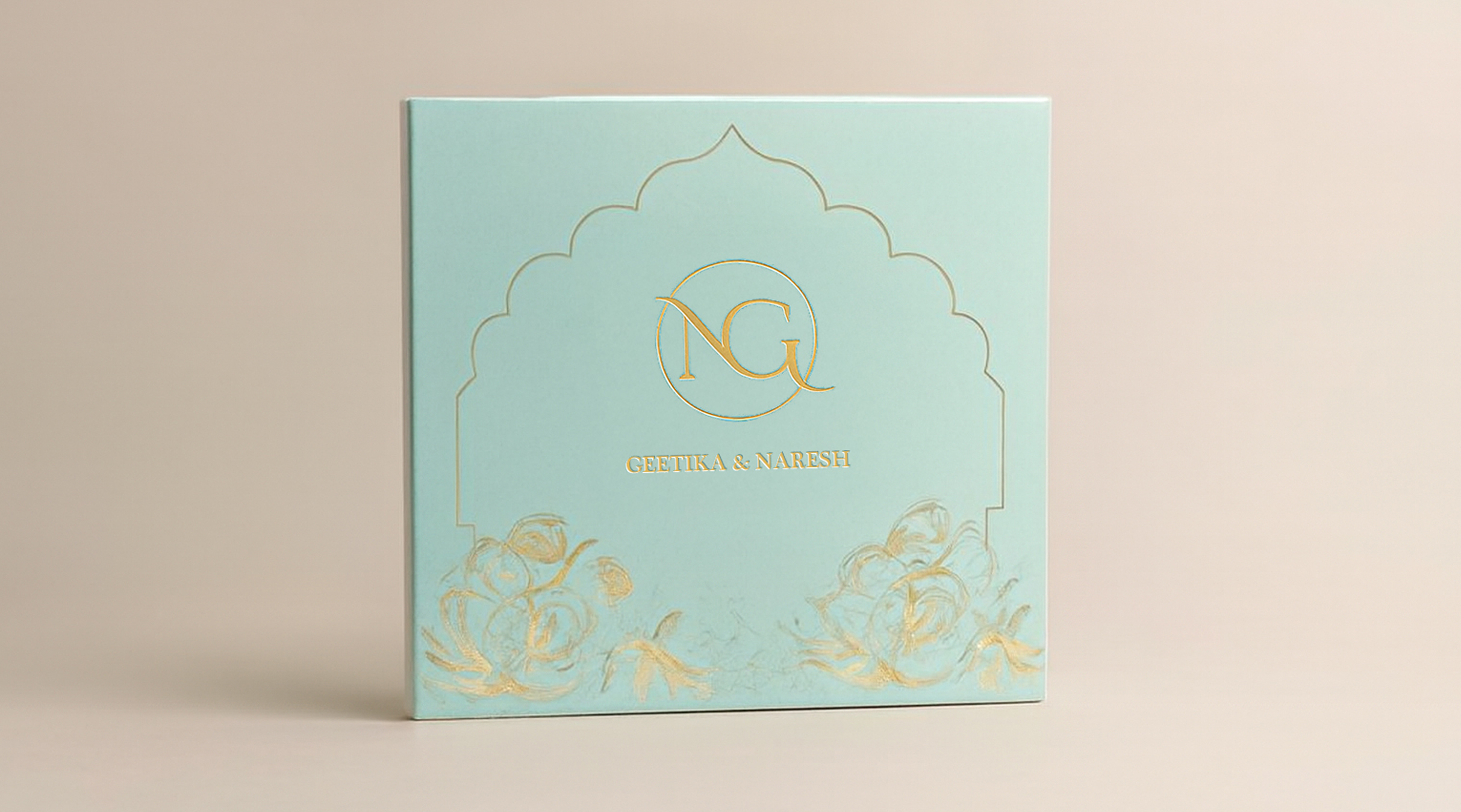 Light blue wedding invitation card with gold floral designs and initials NG above the names Geetika & Naresh.