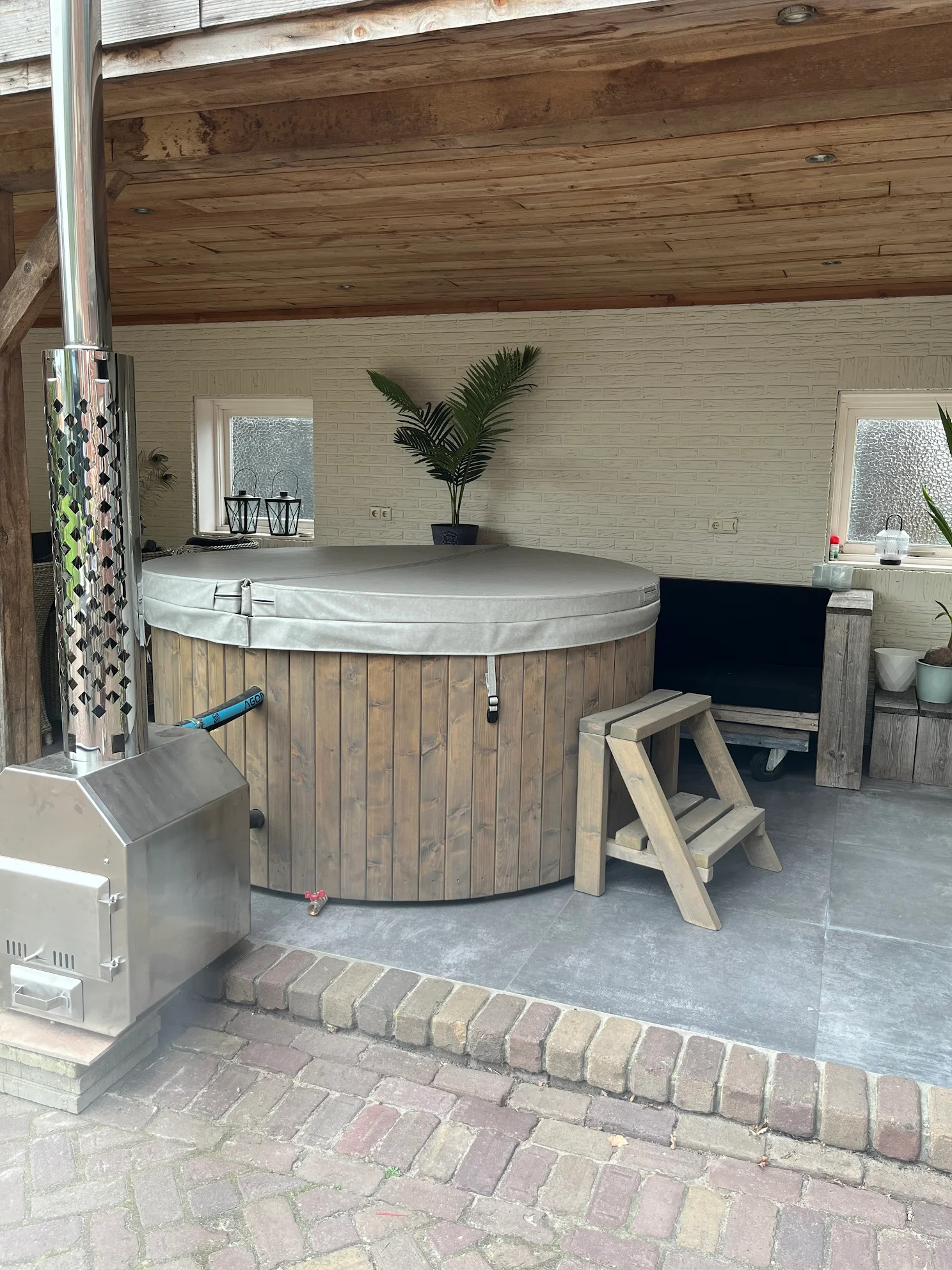 Houten hottub met grijze cover en trapje onder houten overkapping in tuin

