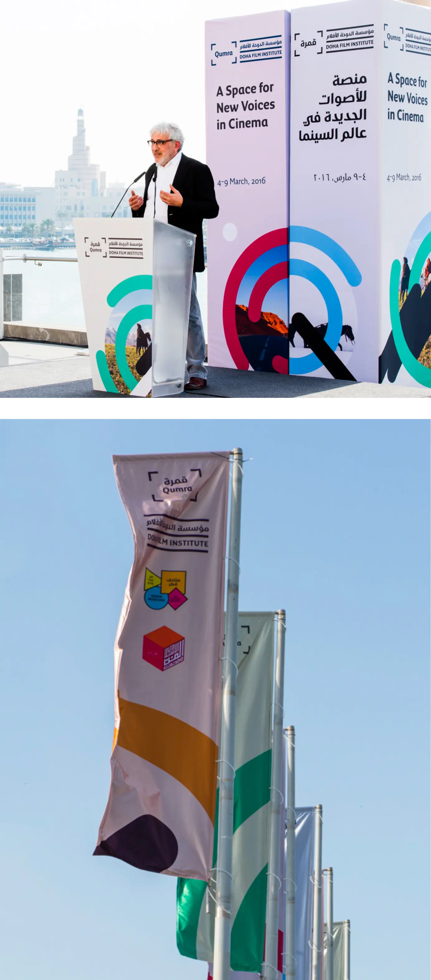 A man speaking at a podium with Doha Film Institute and Qumra branding, next to banners stating 'A Space for New Voices in Cinema' in English and Arabic, and flags with the Doha Film Institute logo fluttering against a clear sky.