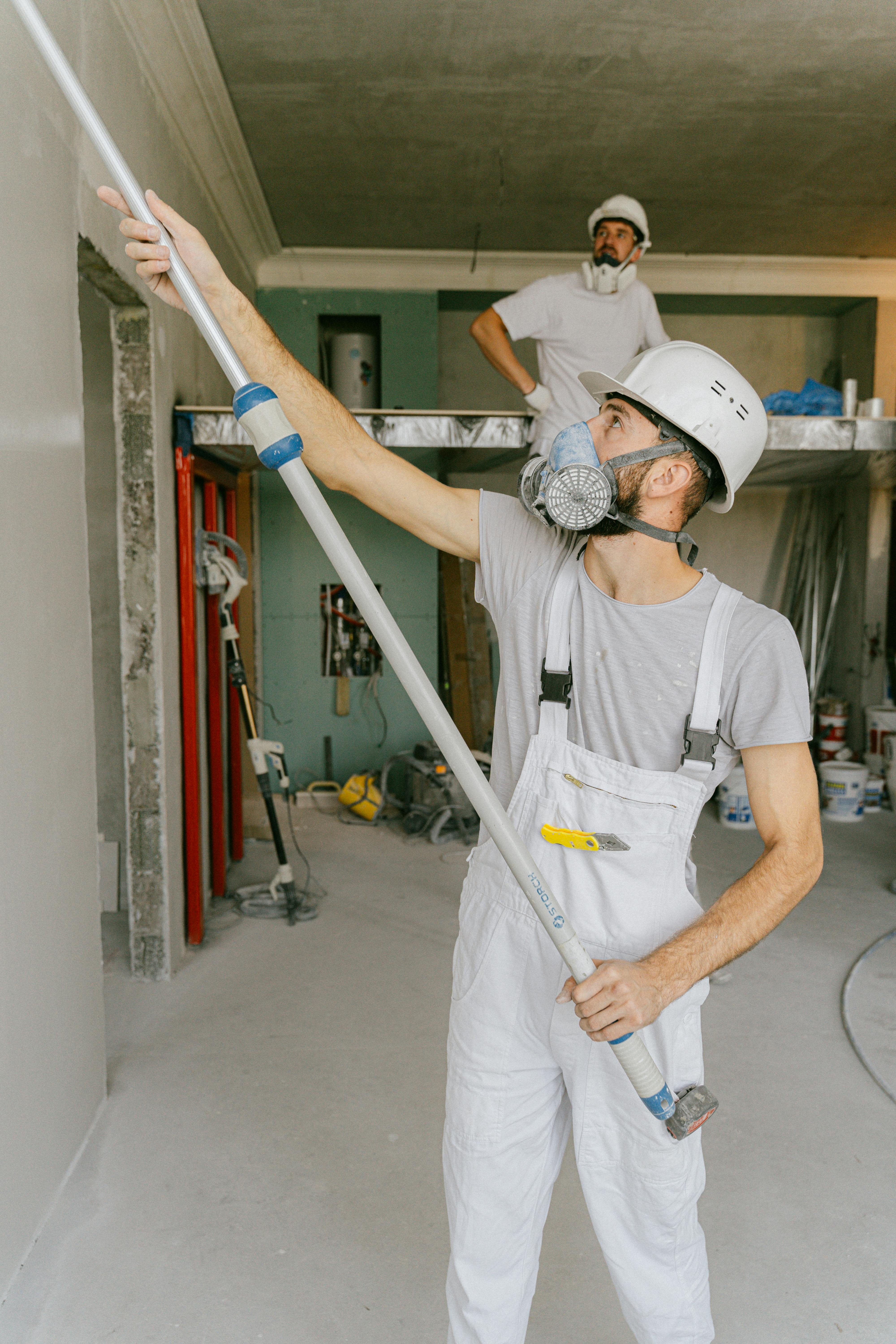 Tradesperson painting walls during a professional home renovation project, wearing safety gear on-site.