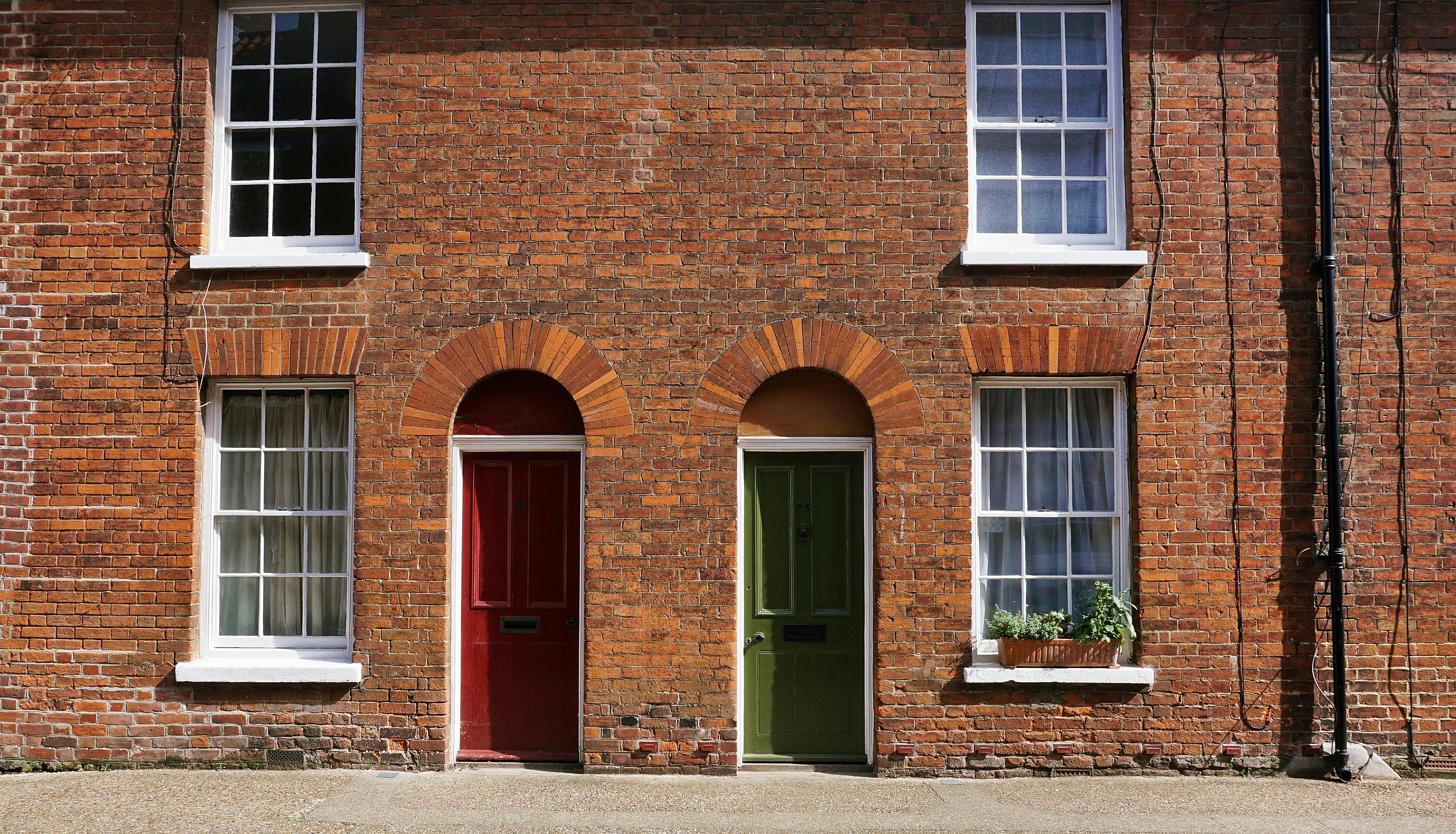 A green and red door as part of a red break terrace house suggesting choose in property sourcing packages