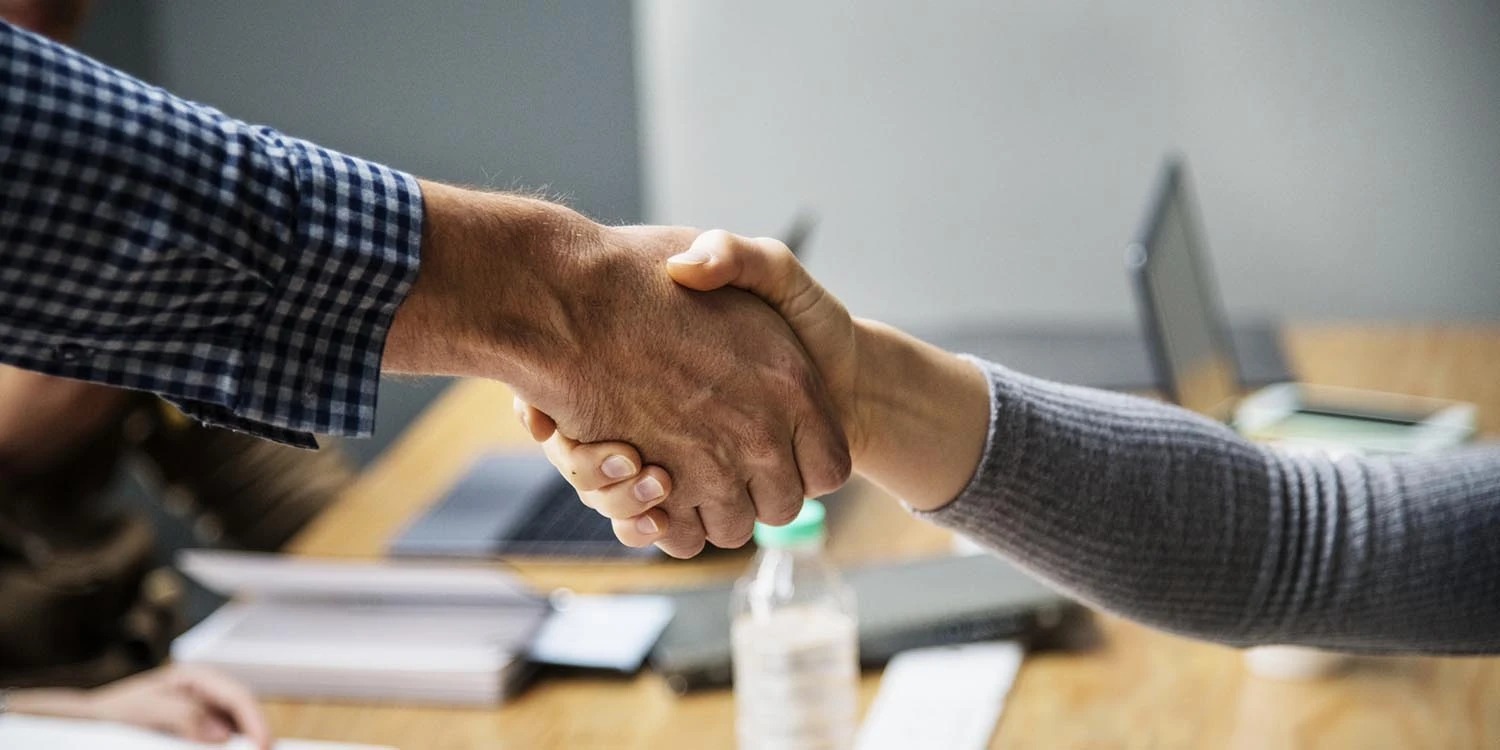 Duas pessoas fazendo um aperto de mãos, simbolizando acordo, parceria ou confiança em um ambiente de trabalho.
